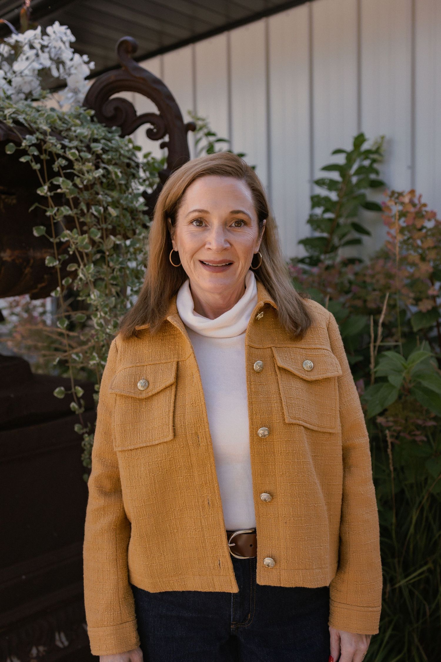Woman wearing a mustard yellow cropped jacket and white turtleneck poses outdoors.