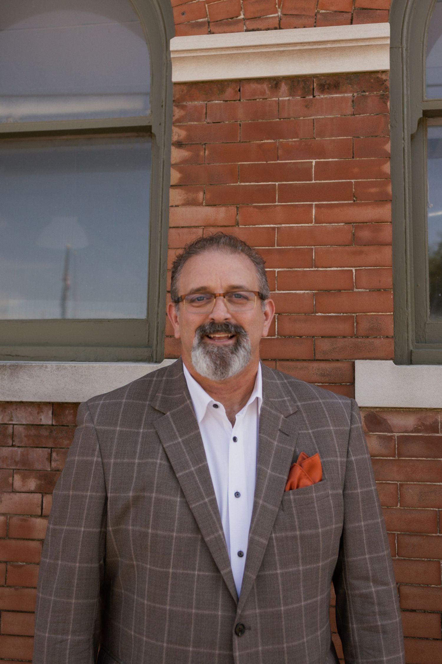 Man wearing gray plaid suit jacket and orange pocket square poses professionally.