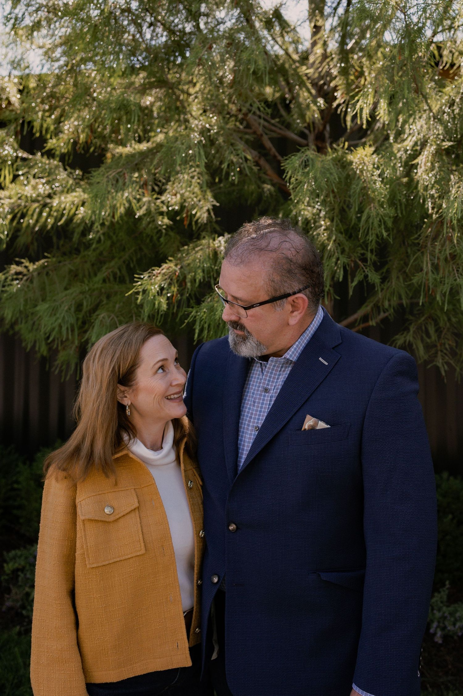 Couple sharing a candid moment while posing outdoors near evergreen trees.