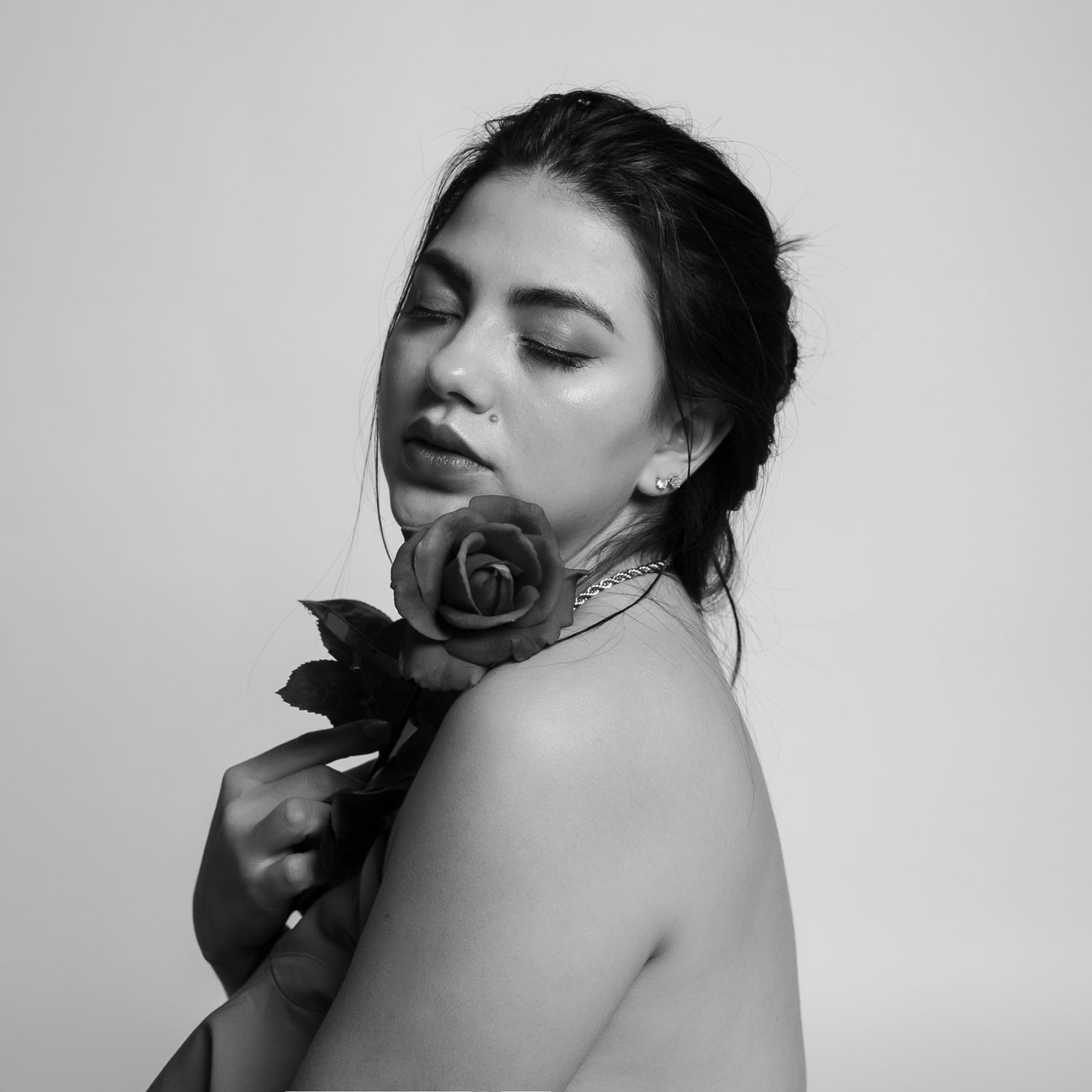 Artistic black and white portrait of a woman posing with a rose against neutral background.