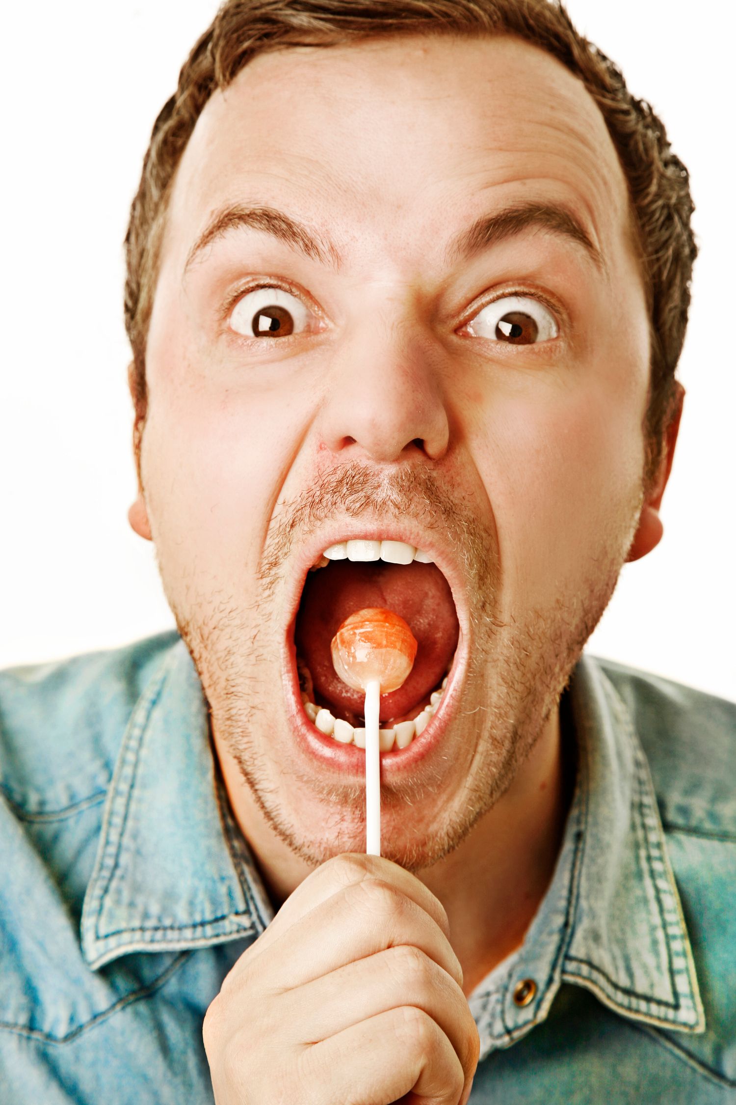 Person with wide eyes holding a lollipop in their mouth while wearing denim jacket.