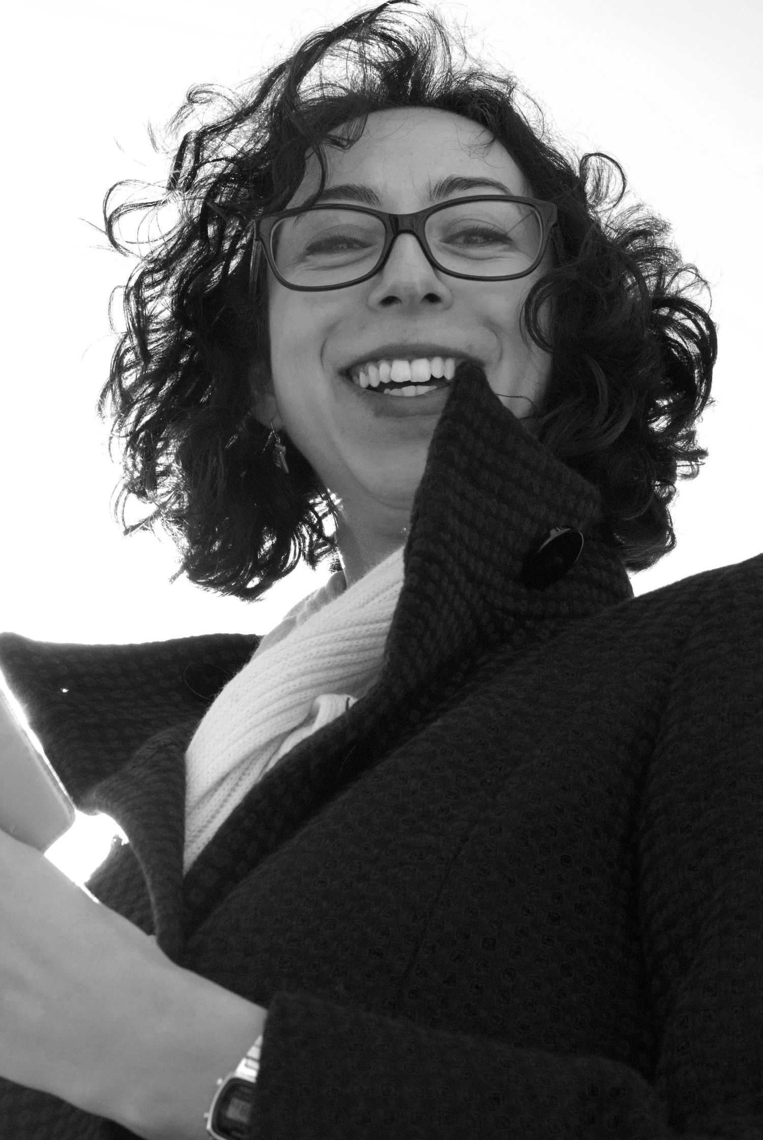 Black and white portrait of a person with curly hair laughing while wearing glasses.