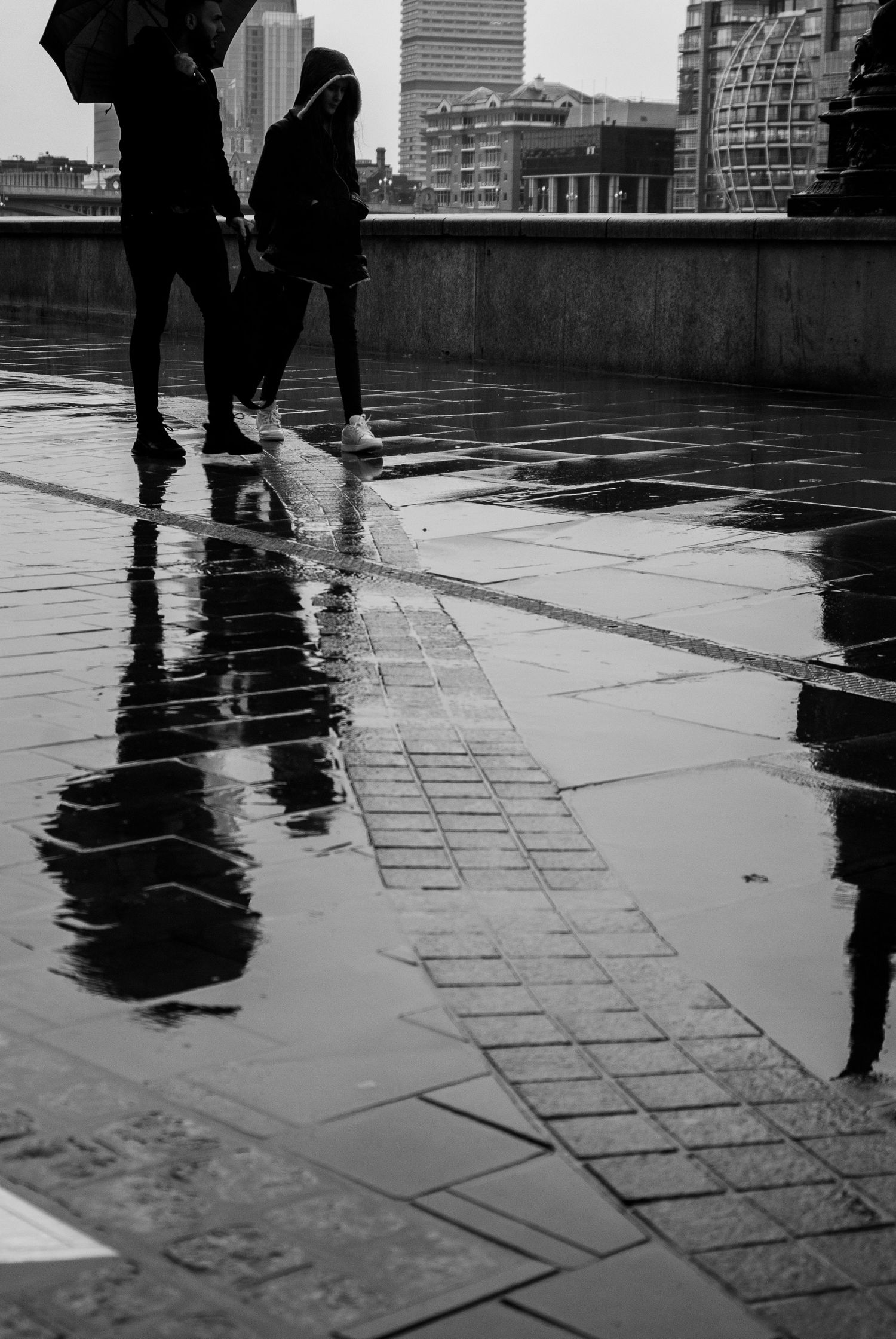 Black and white reflections of pedestrians on wet pavement during a rainy day in the city.
