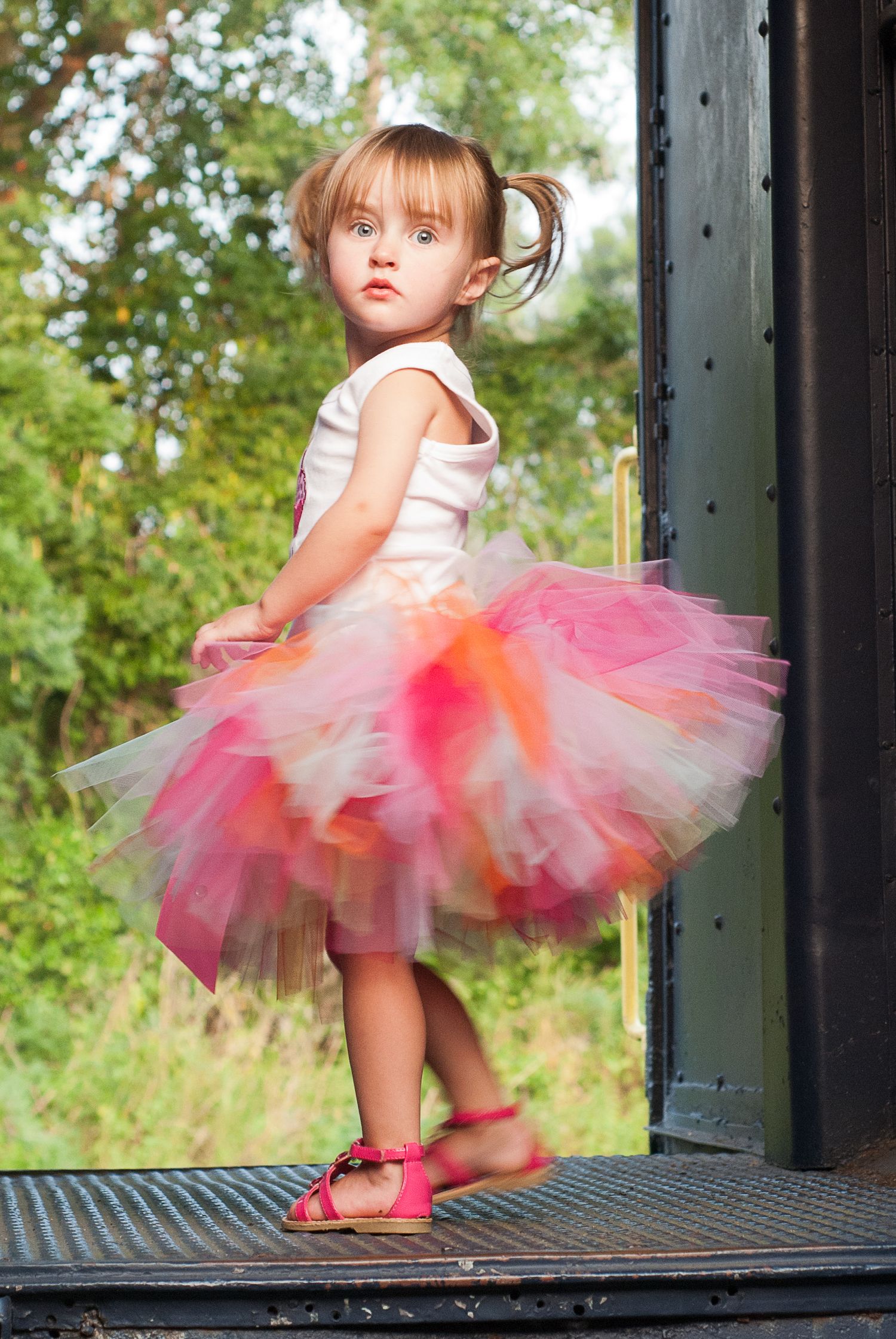 Young dancer in a pink and white tutu twirls on a dark platform outdoors.