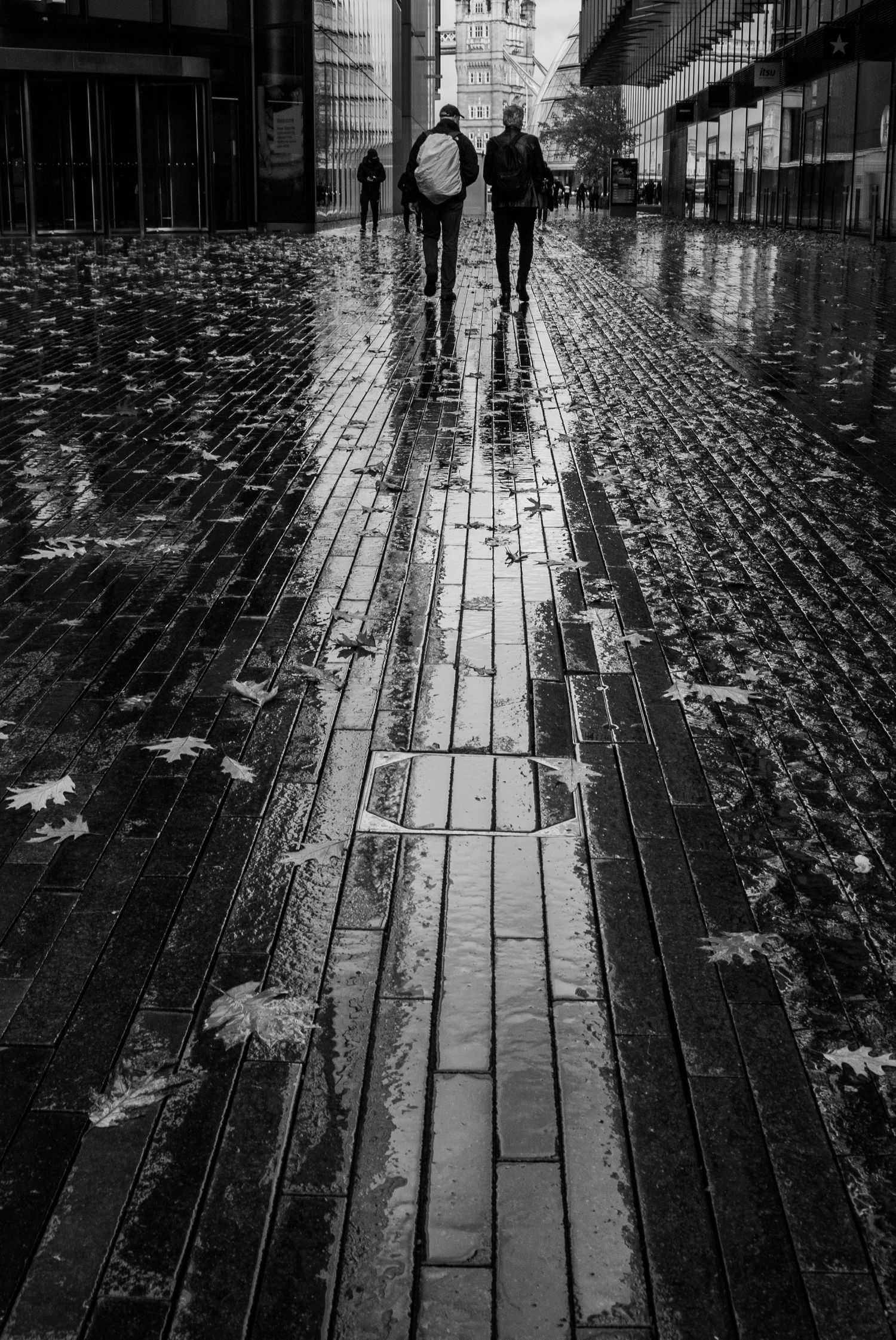Wet cobblestone street with pedestrians walking in rain toward distant buildings.