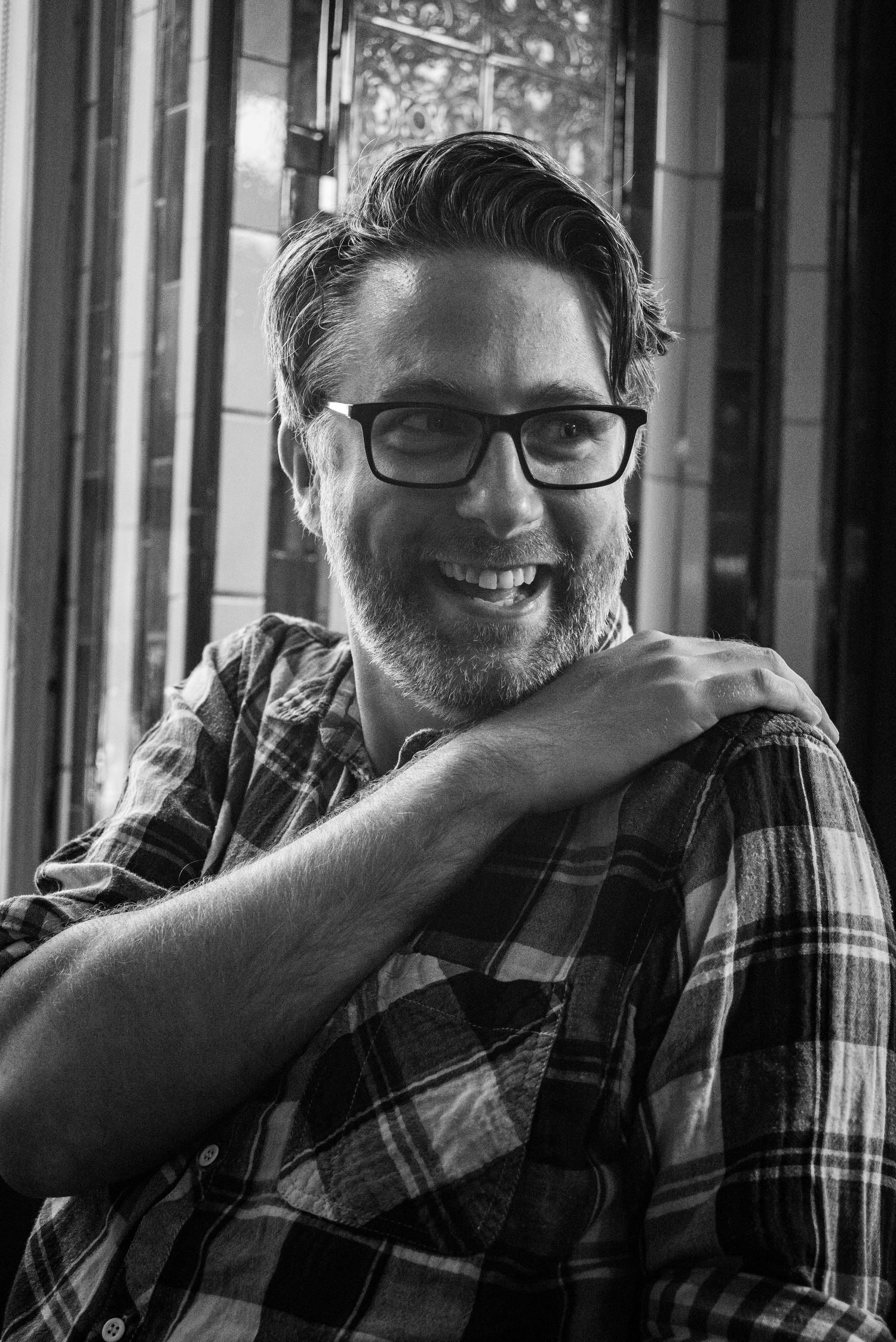 Black and white portrait of smiling man in plaid shirt and glasses.