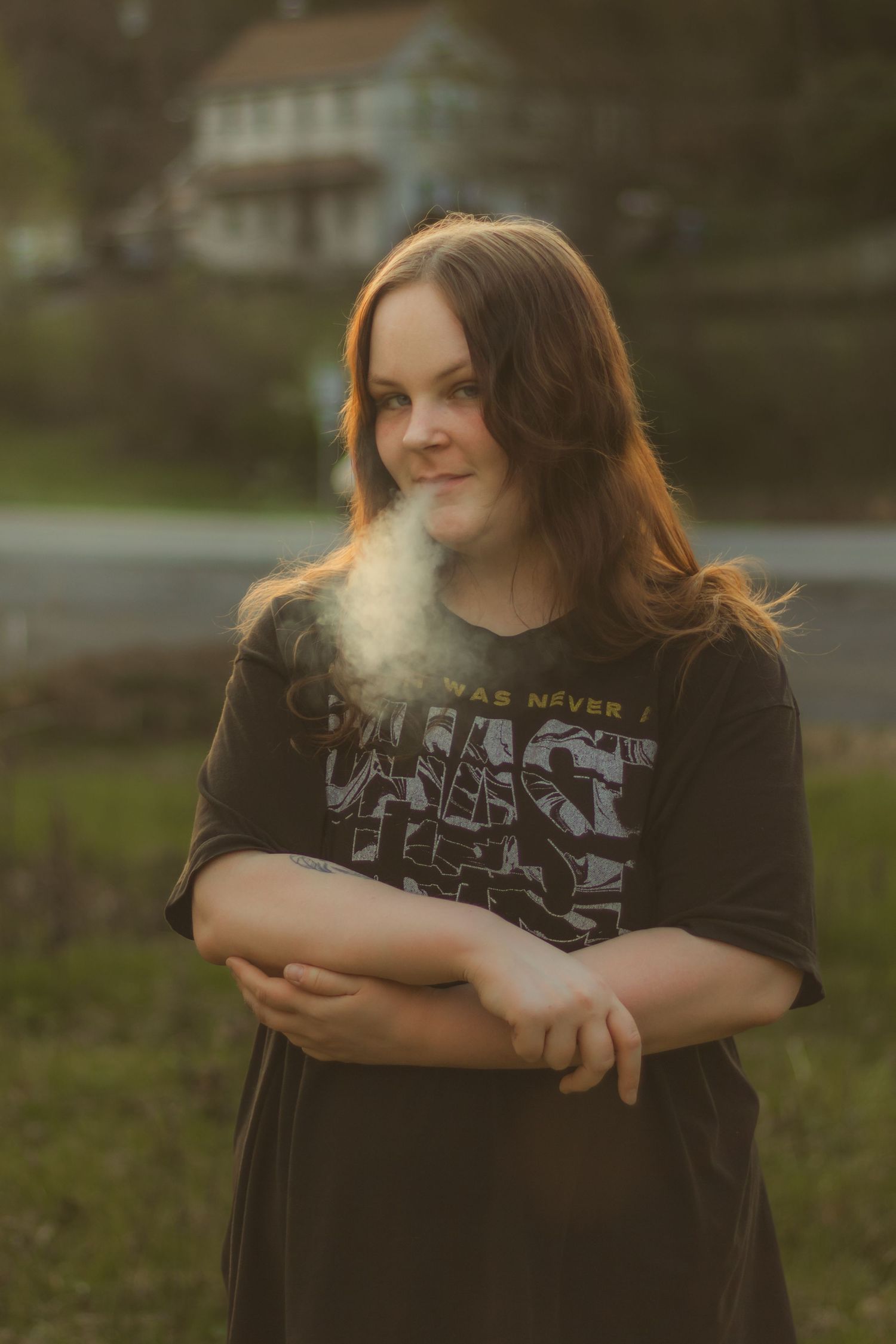 Young woman in graphic tee stands outdoors at golden hour with breath visible in cool air.