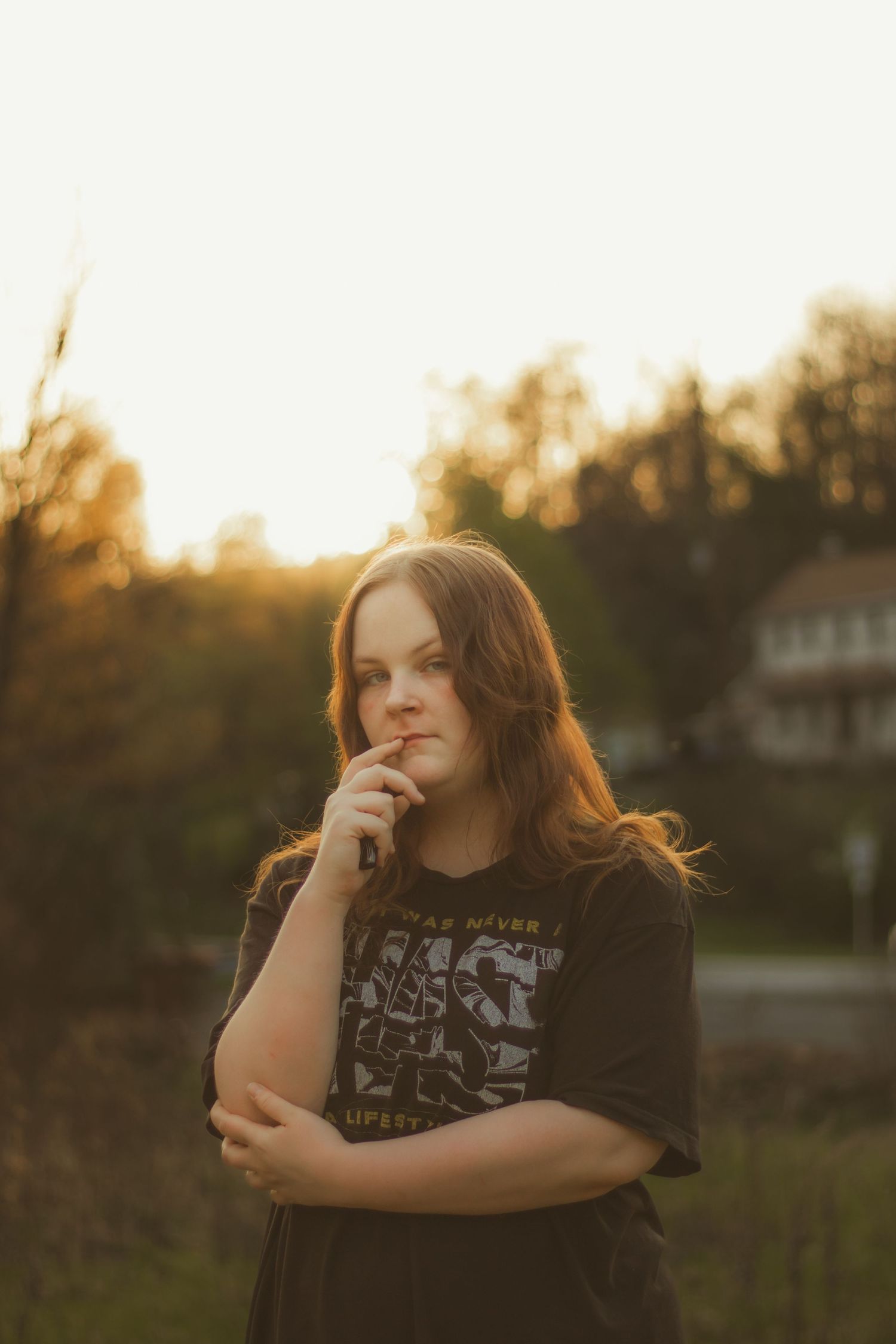 Young woman in graphic tee poses thoughtfully outdoors during golden hour sunset portrait session.