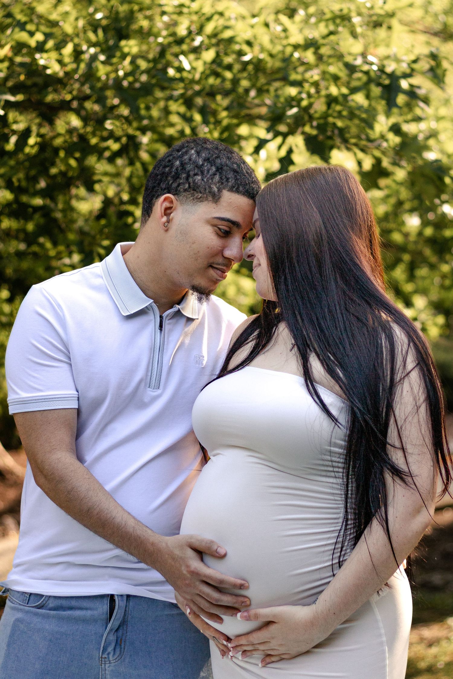 A couple sharing a tender moment outdoors, with the man gently holding his pregnant partner's baby bump.