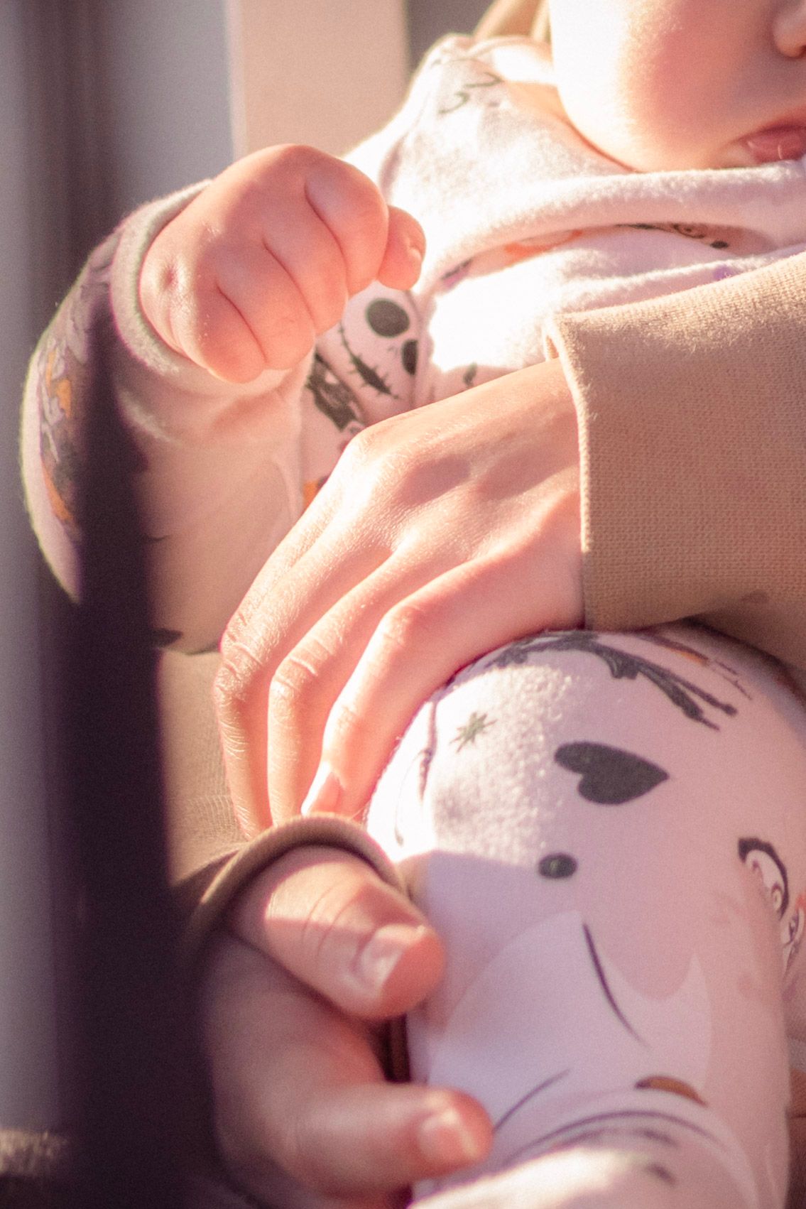 Close-up of adult hands gently holding a baby dressed in panda print outfit in sunlight.