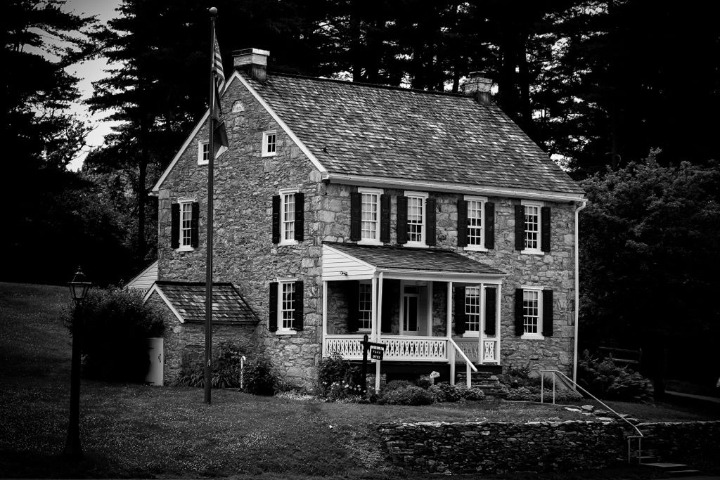 A classic colonial stone house with black shutters photographed in black and white.