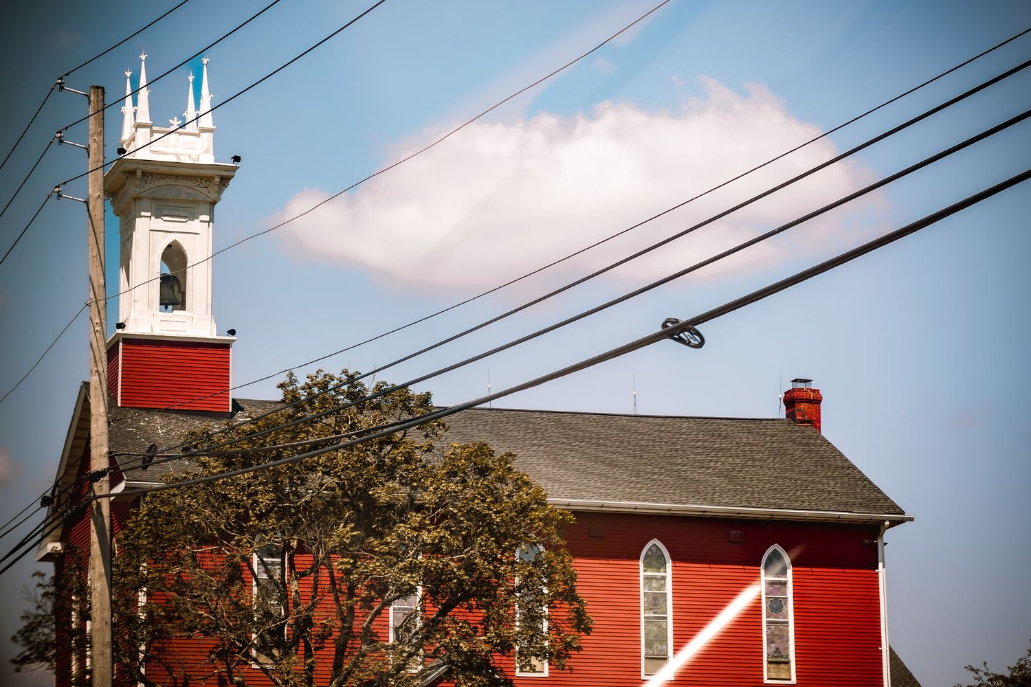 A red historic church with white steeple and Gothic windows beneath a partly cloudy sky.