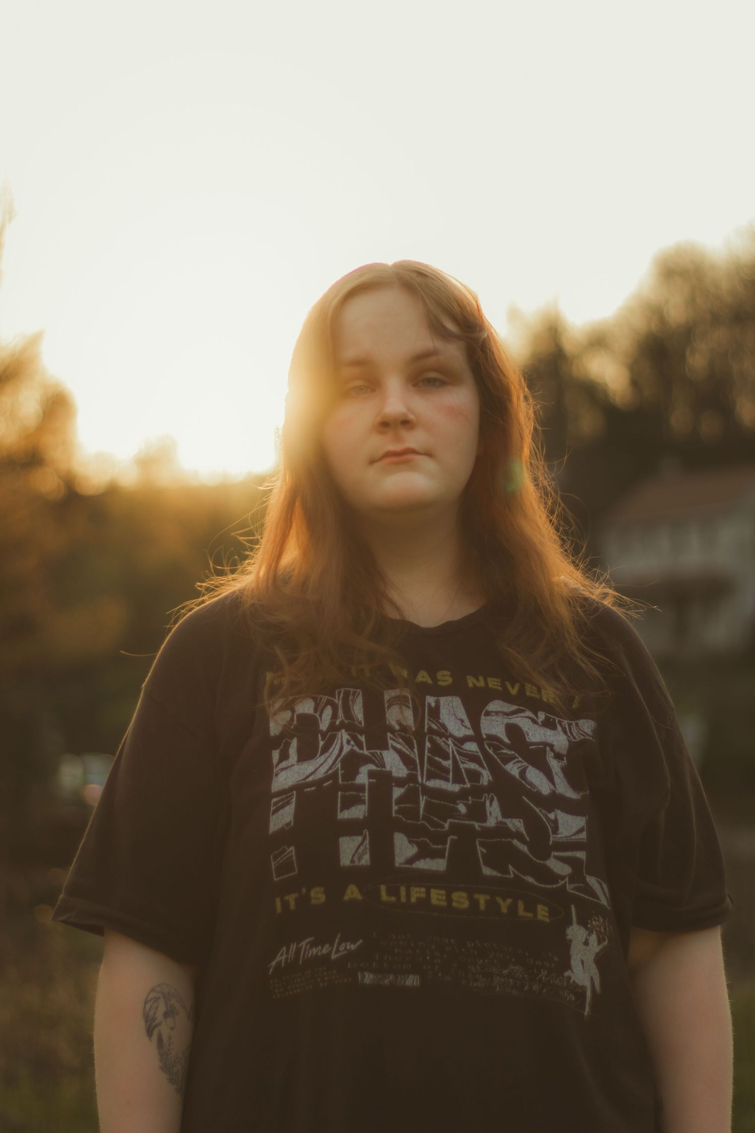 Young woman with long auburn hair gazes directly at camera during a warm golden hour outdoor portrait session.