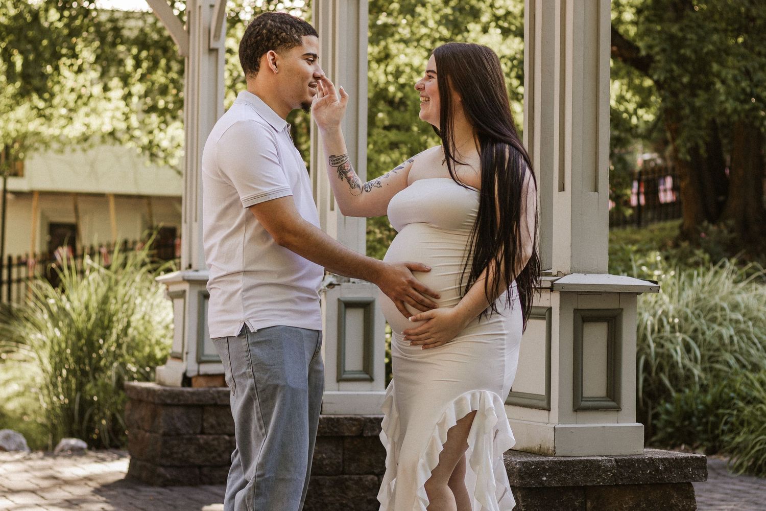 Couple sharing a tender moment outdoors, man gently touching pregnant woman's face in a lush garden setting.