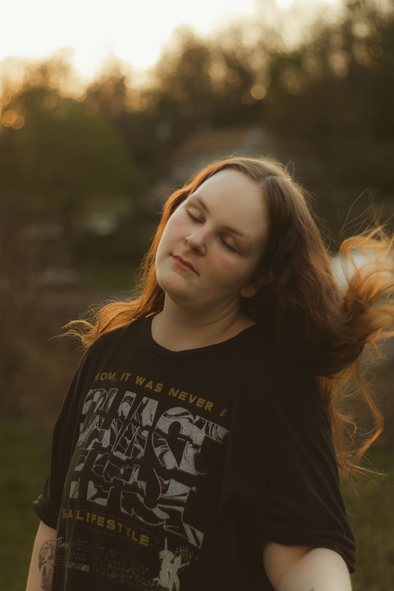 Woman with flowing auburn hair closes her eyes peacefully during a warm sunset photoshoot in a natural outdoor setting.