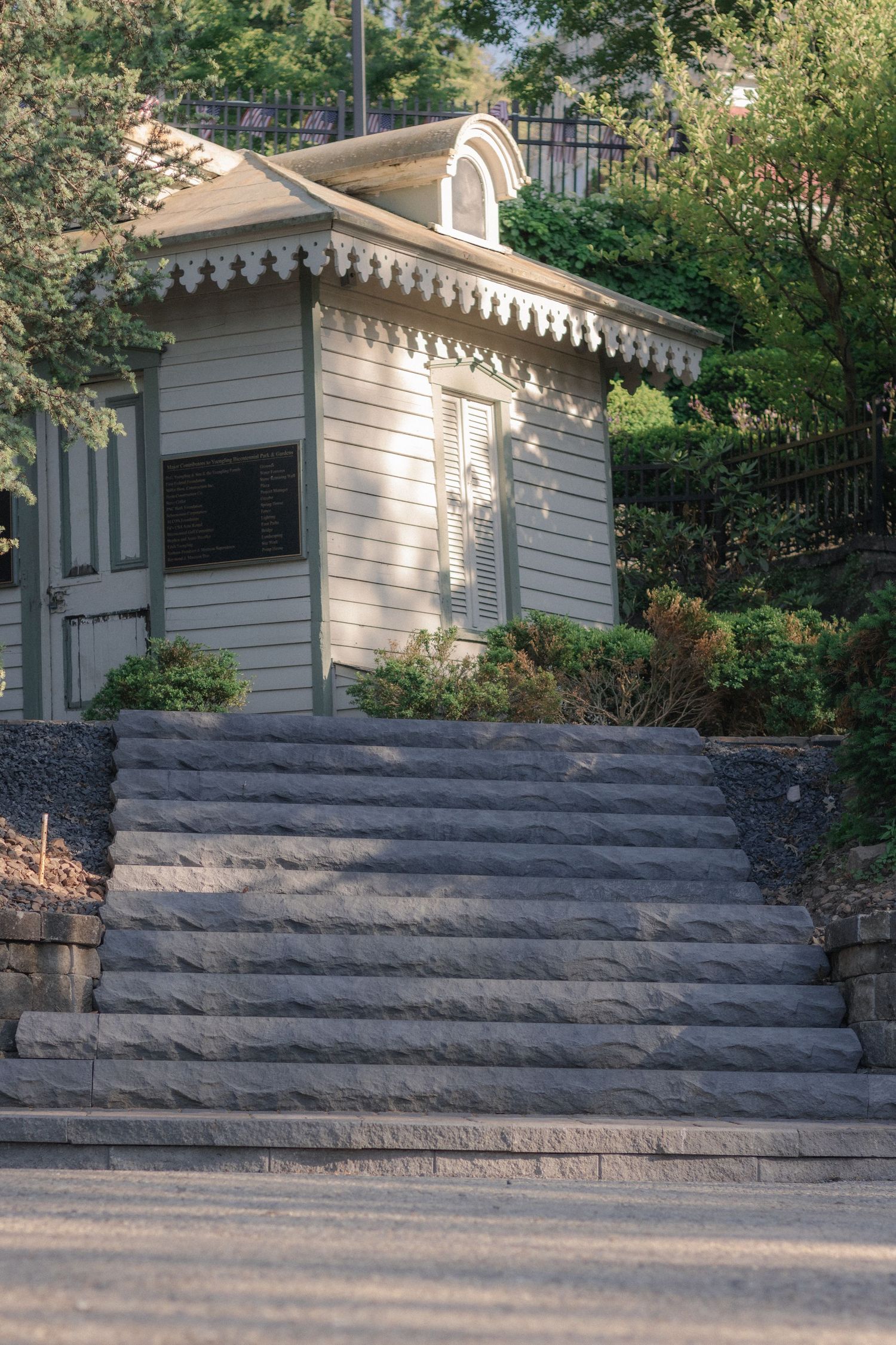 Historic white wooden gazebo with decorative trim atop stone steps surrounded by lush greenery.