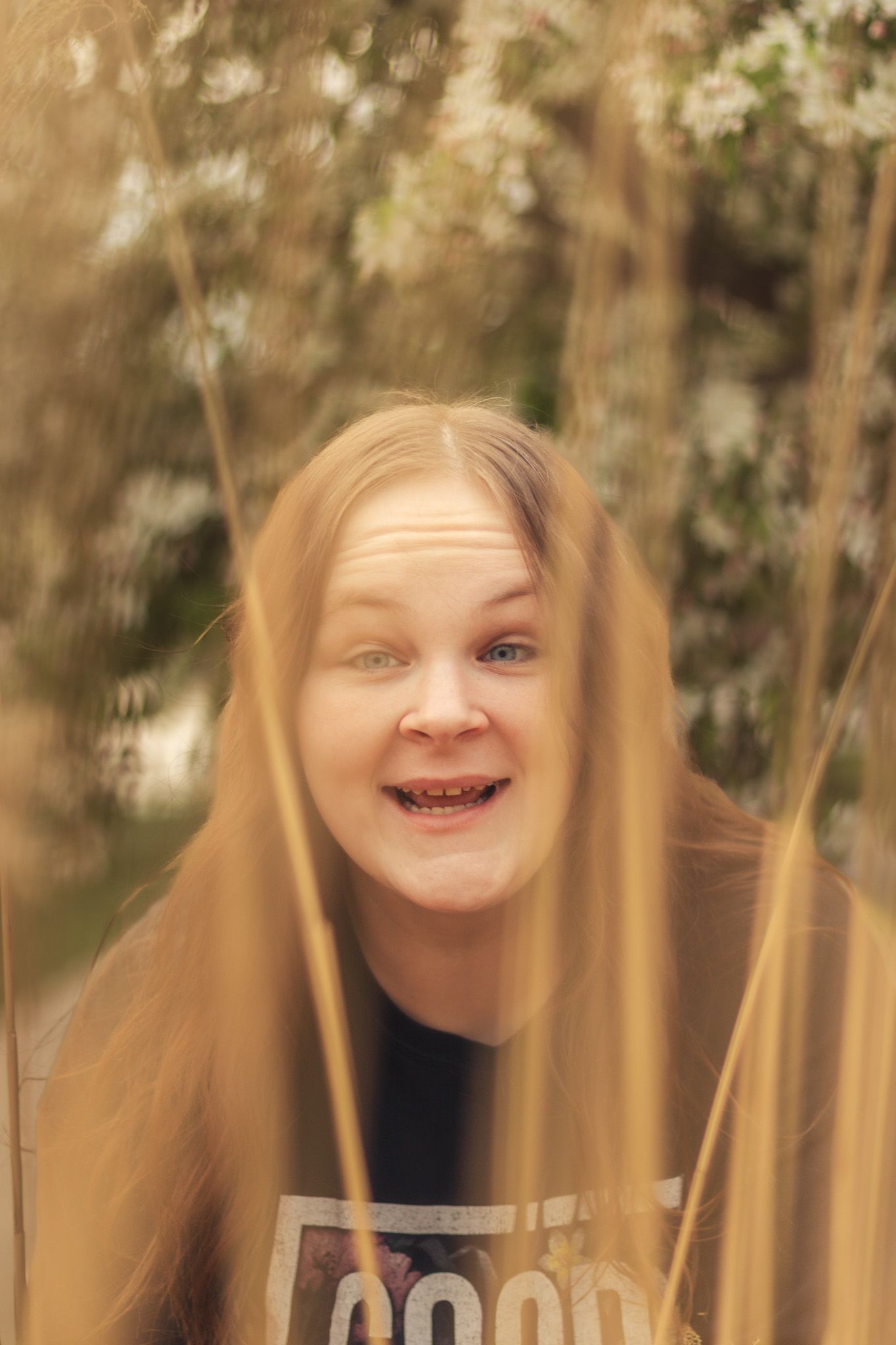 Laughing Brown-haired woman peers through tall golden grass in a sun-drenched outdoor setting.