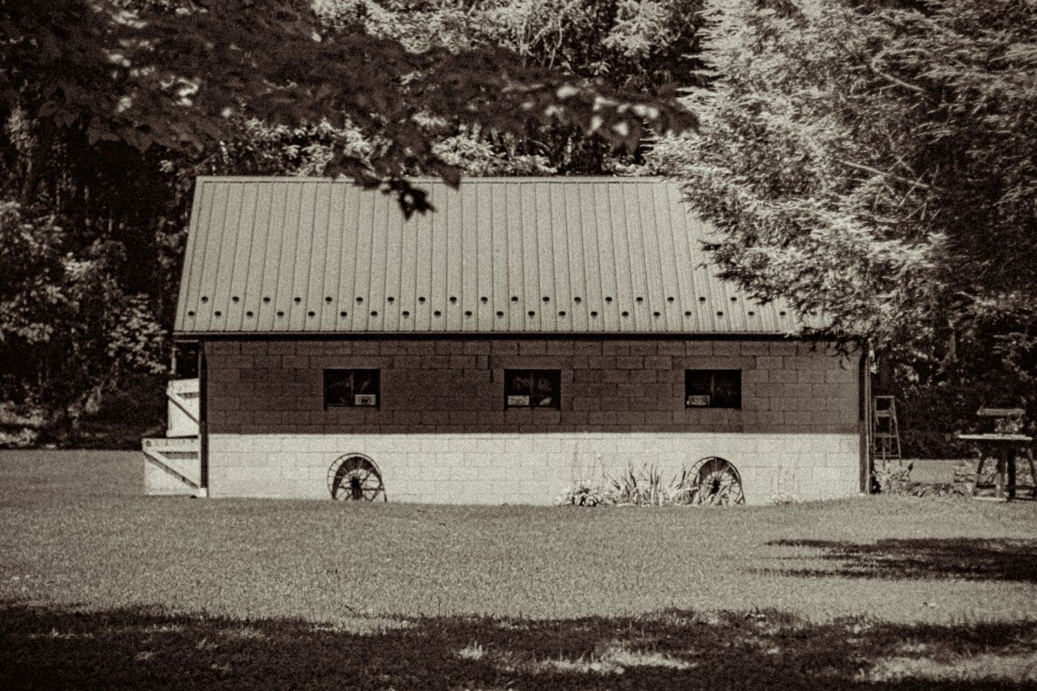 Vintage sepia-toned photo of a rustic barn with wagon wheels and metal roof in a field.