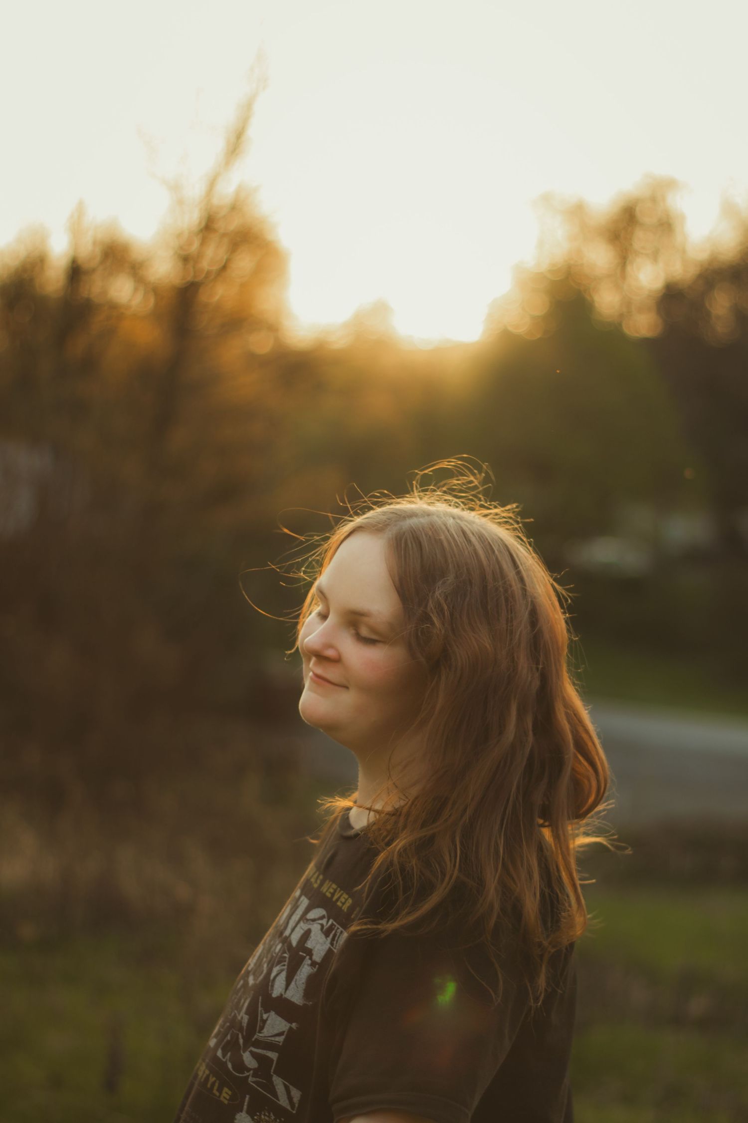 Young woman with long brown hair smiling outdoors during golden hour sunset with warm backlight.