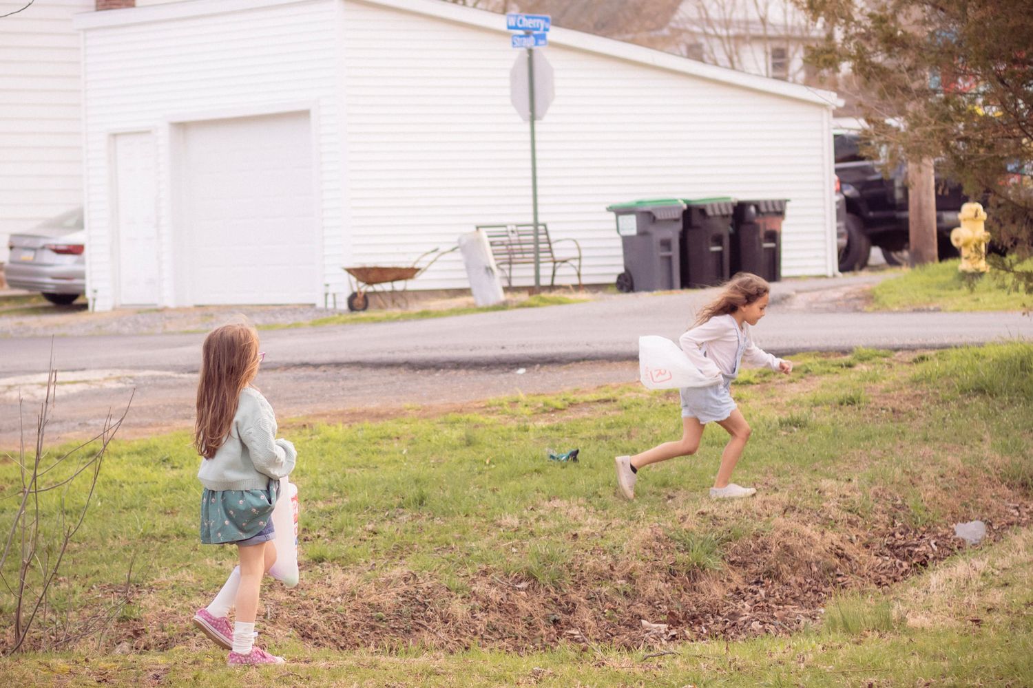 Two young girls running and playing on a grassy lawn in a residential neighborhood during daytime.