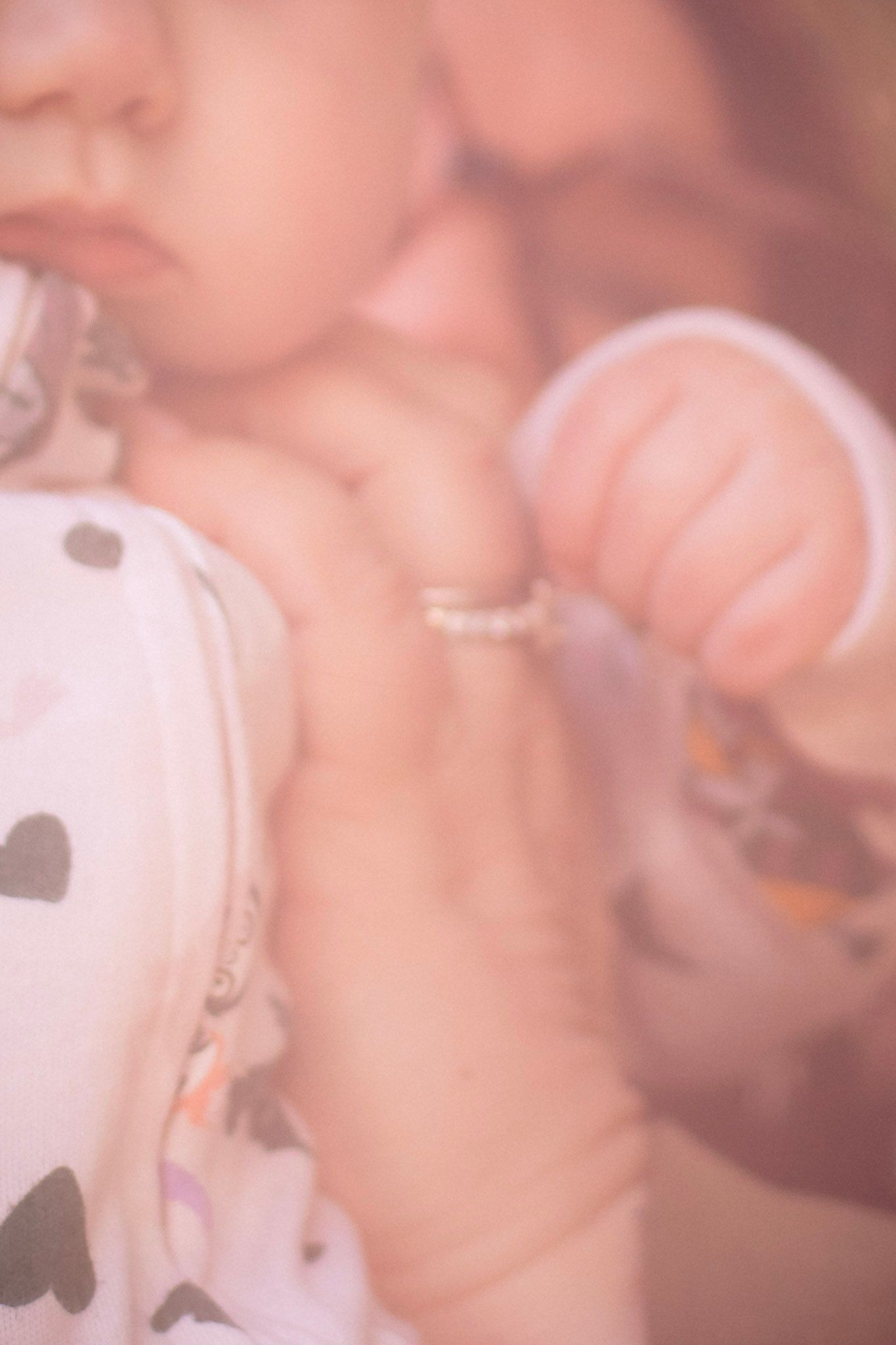 Soft blurred close-up of mother kissing baby wearing heart print outfit with pearl bracelet.