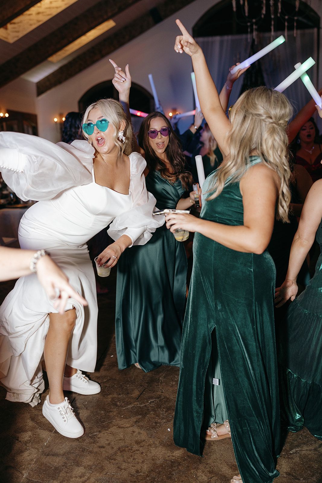 Wedding party dancing with glow sticks, featuring bridesmaids in emerald green dresses.