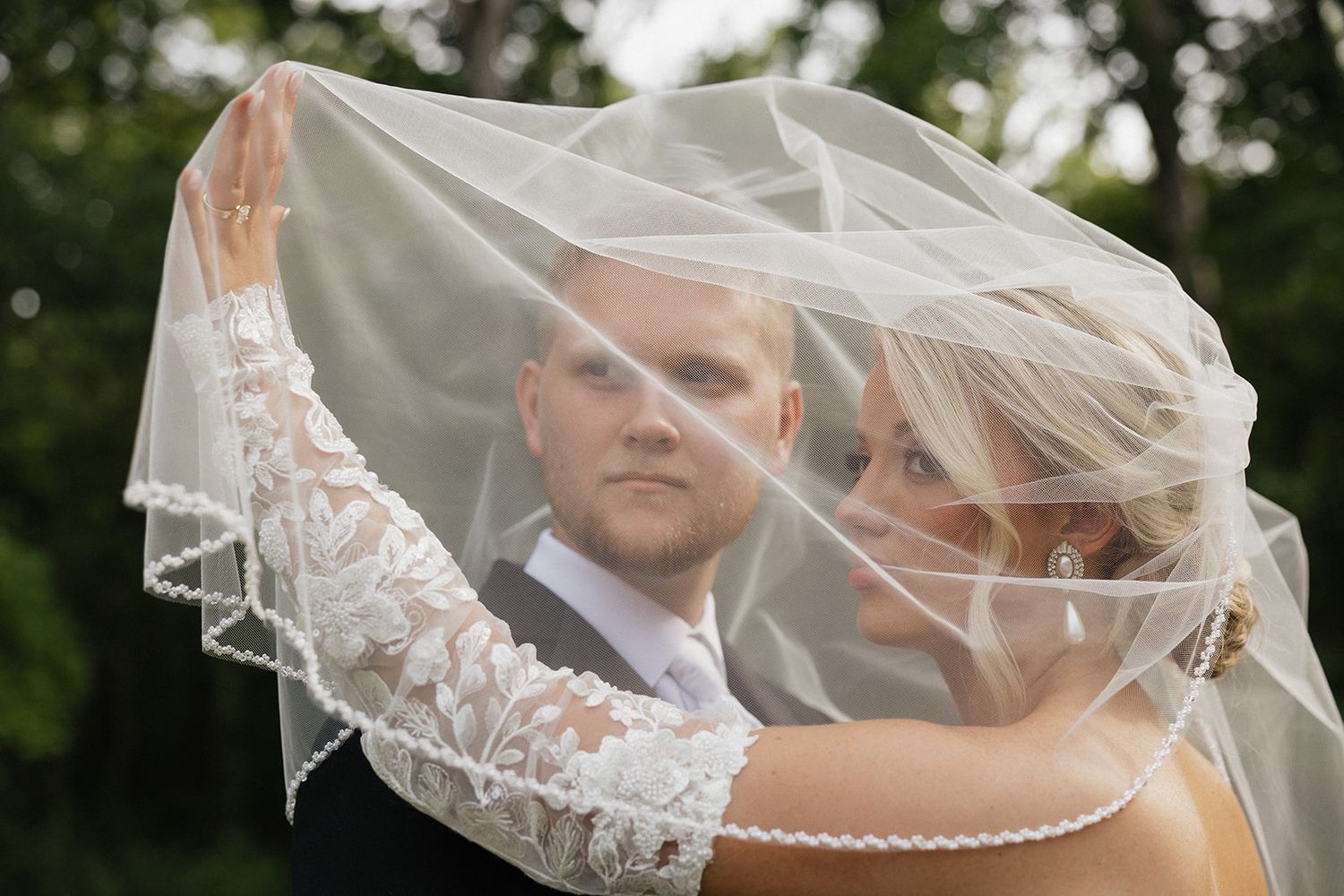 Romantic wedding portrait with bride's veil floating in breeze as couple embraces.