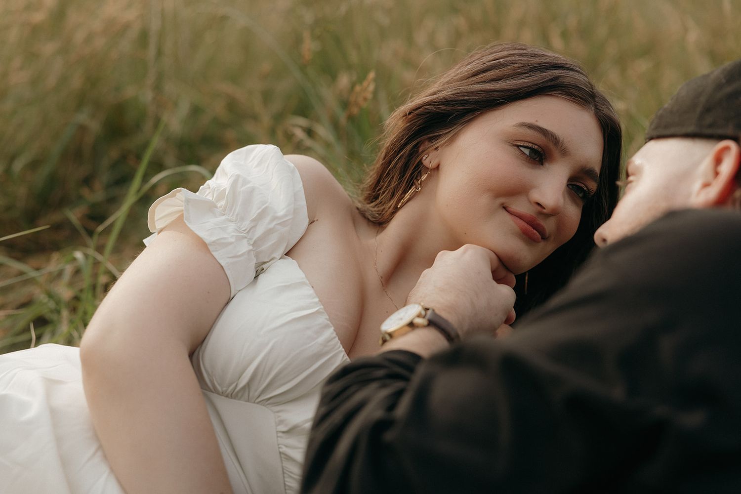 A romantic couple shares an intimate moment in a field of tall grass as the woman in a white dress leans close.