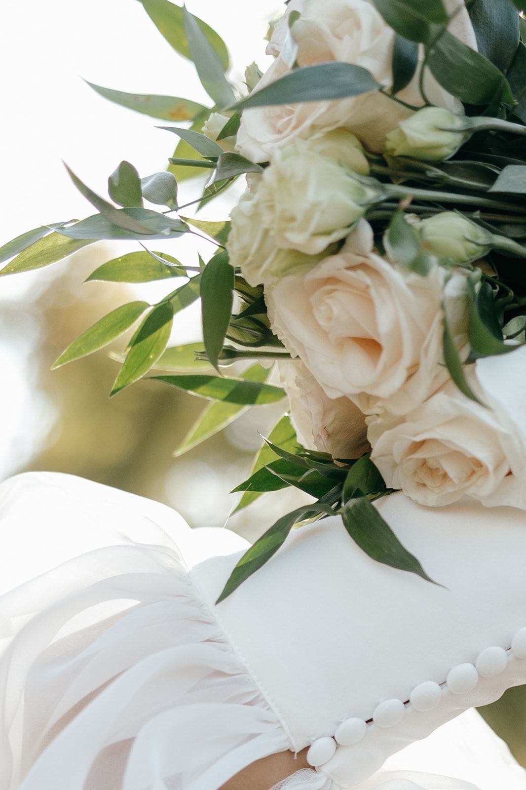 Elegant white roses and greenery bouquet against white fabric background.