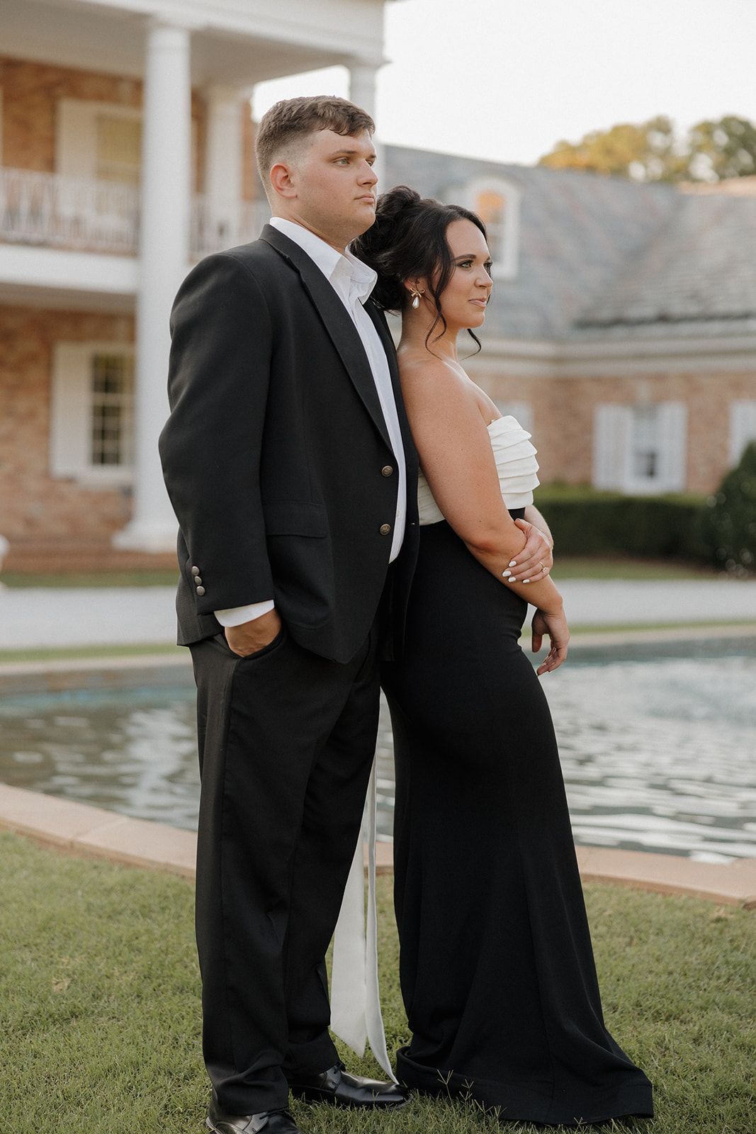 Wedding party members pose by a reflecting pool outside an elegant brick building.