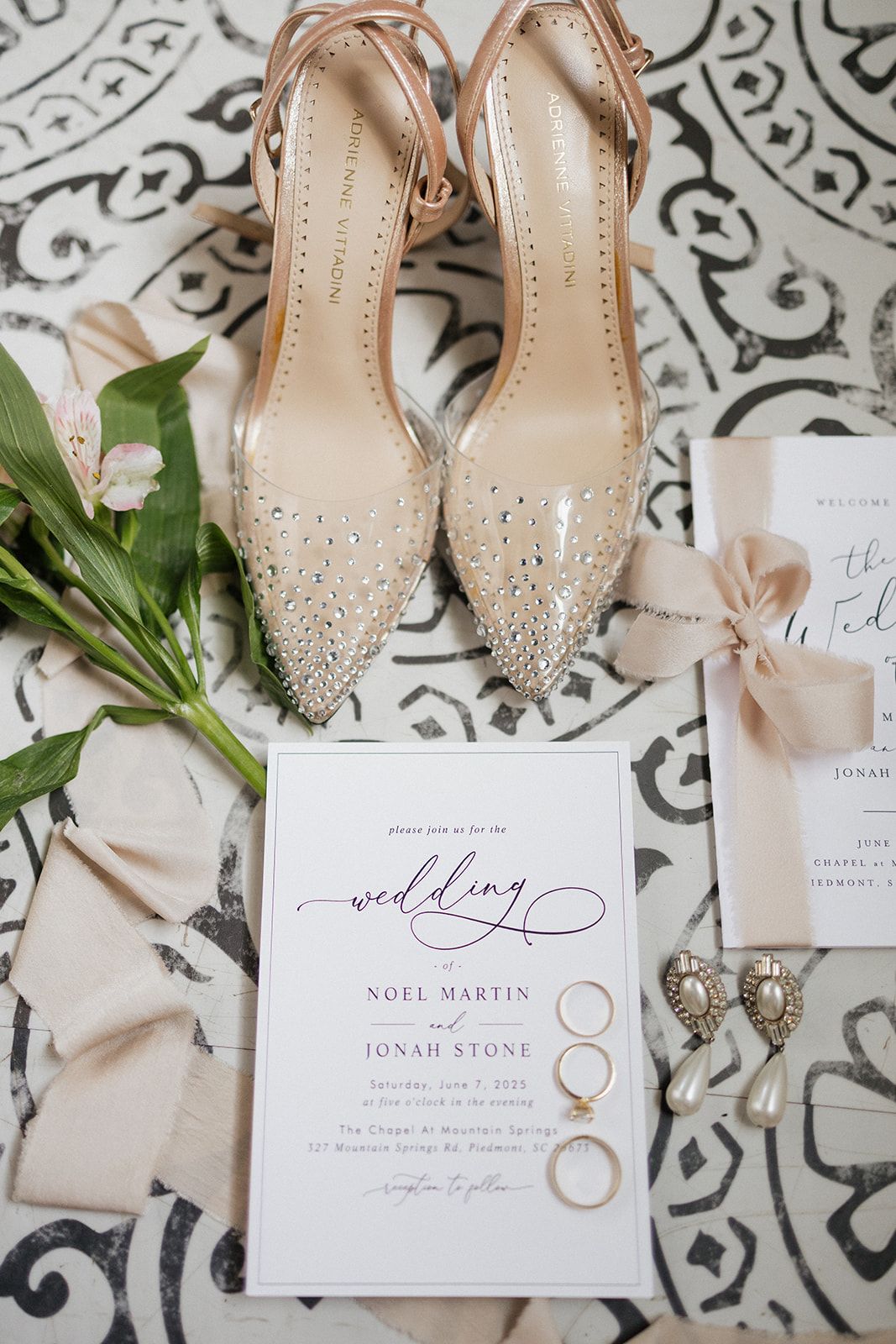 Wedding details flat lay with sparkly heels, invitation suite, and gold rings on patterned background.