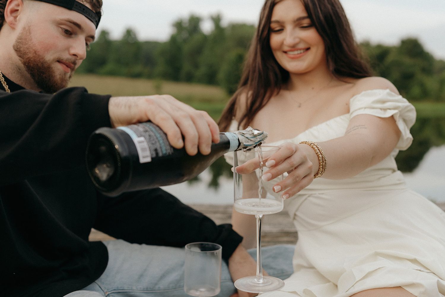 A couple enjoys a romantic picnic outdoors as they pour drinks together on a sunny day.