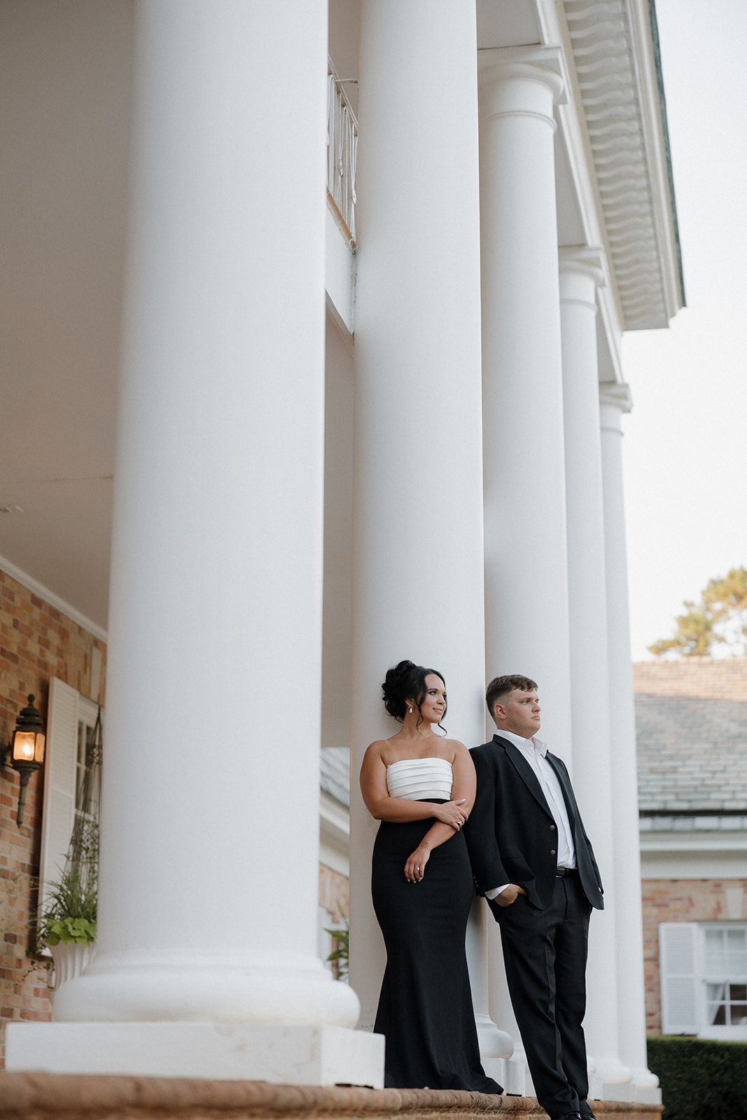 Elegant couple poses between grand white columns in formal evening attire.