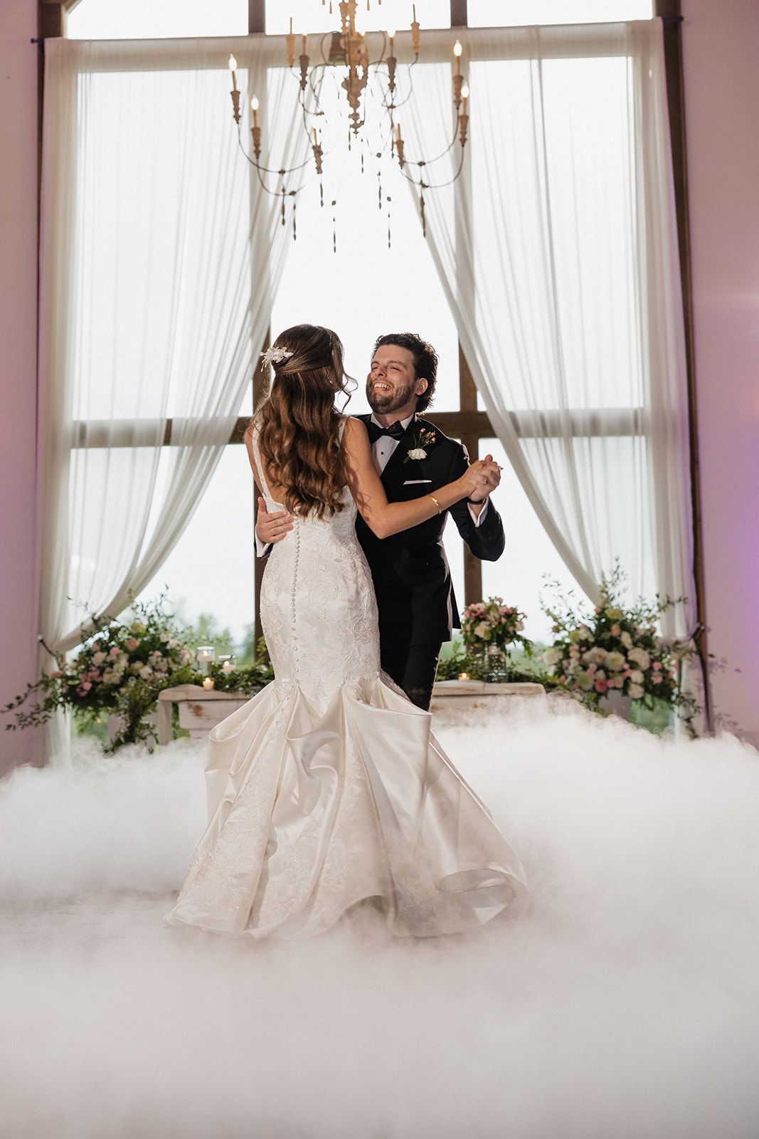 Bride and groom share romantic dance moves in an elegant room filled with ethereal fog and soft window light.