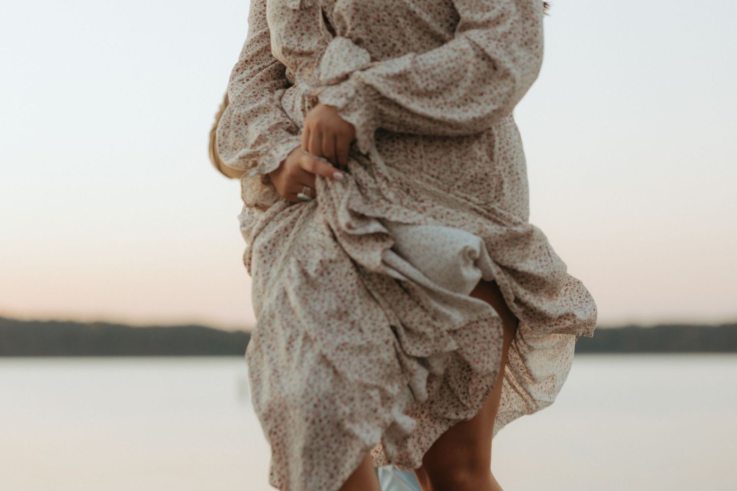 Close-up of flowing beige dress fabric against sunset lake backdrop.