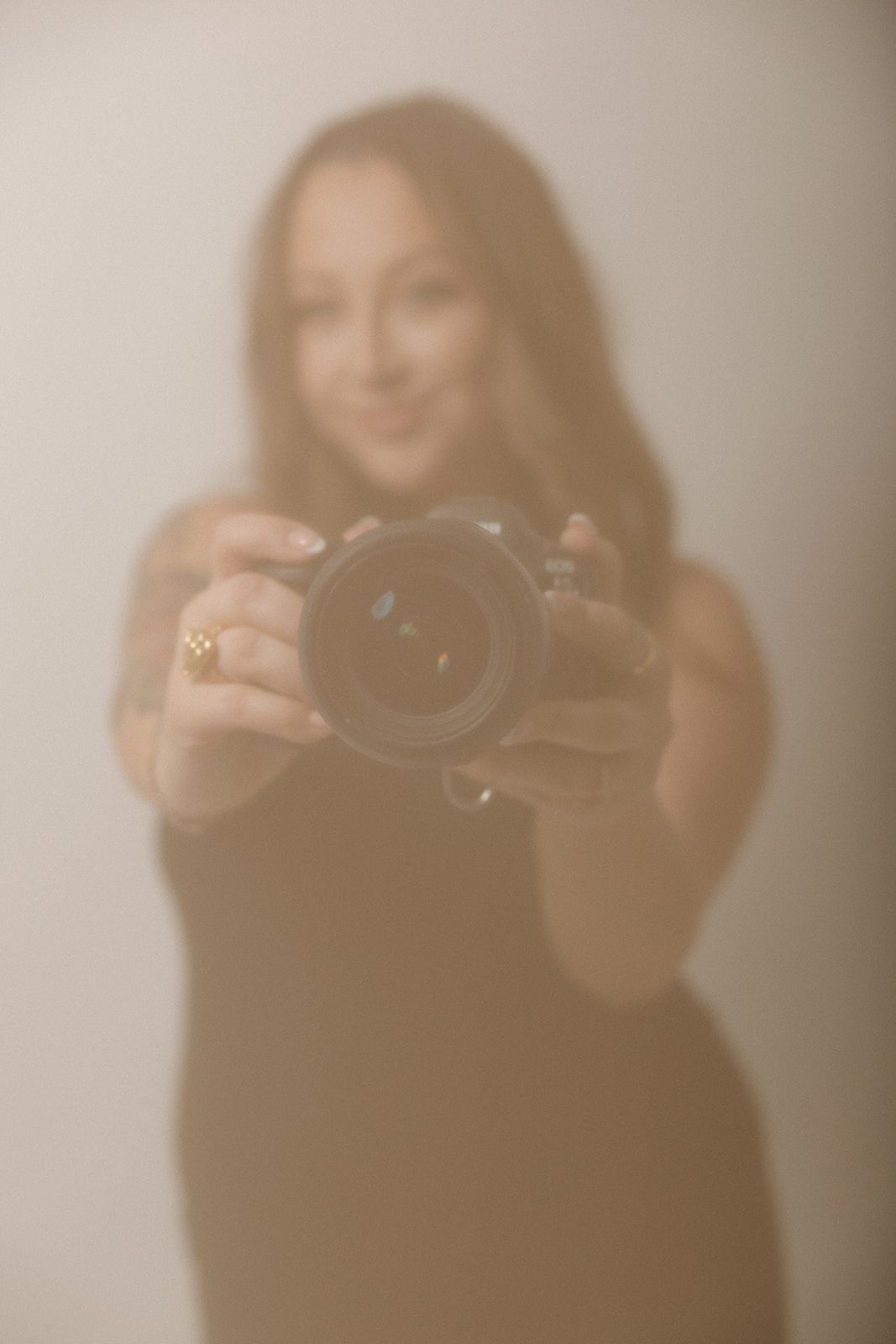 Four soft-focused images show a photographer in black holding a camera in various poses against a neutral background.