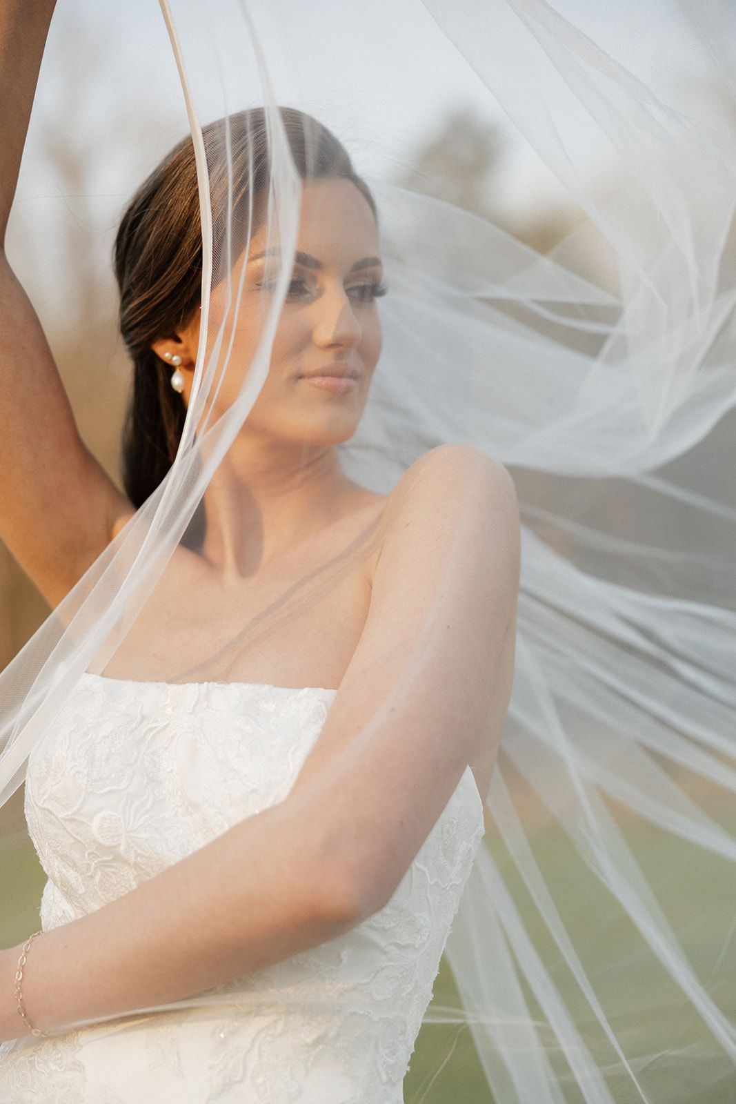 Artistic bridal portrait with flowing veil catching wind and sunlight.
