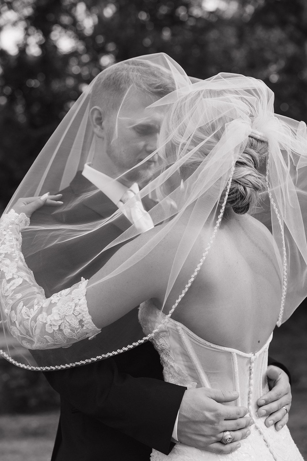 Romantic black and white portrait of couple embracing under flowing wedding veil.