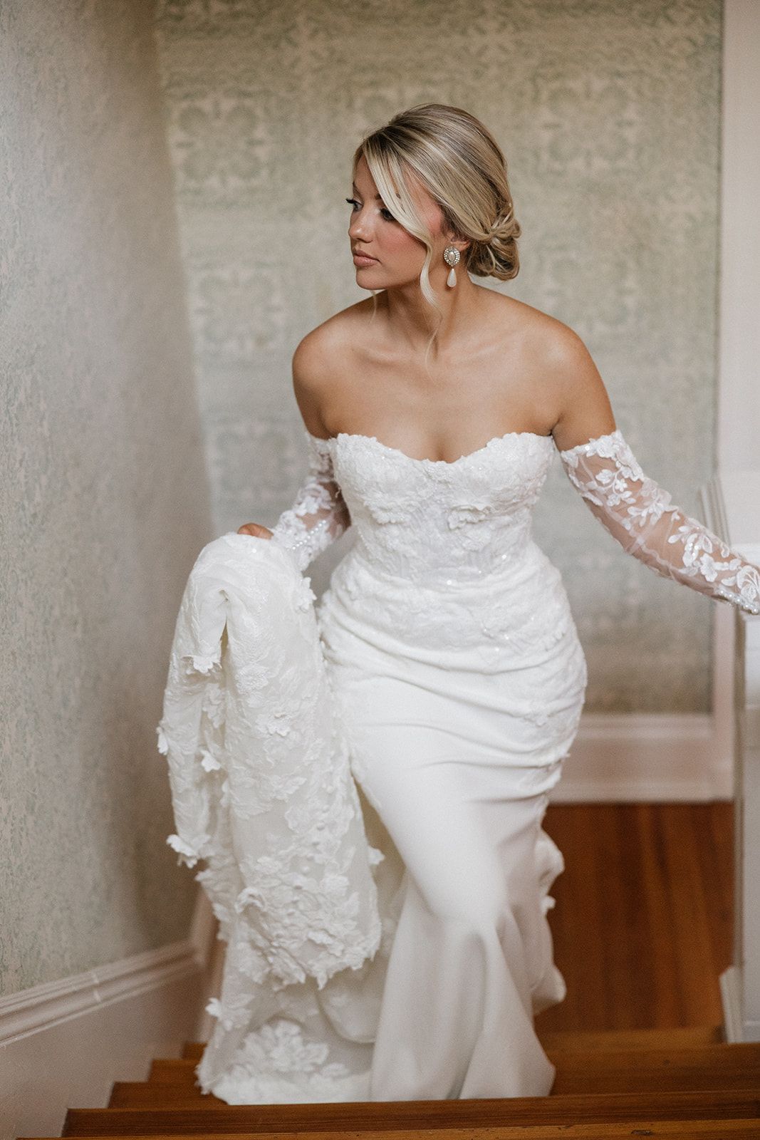 Bride in fitted lace gown ascending staircase in elegant pose.