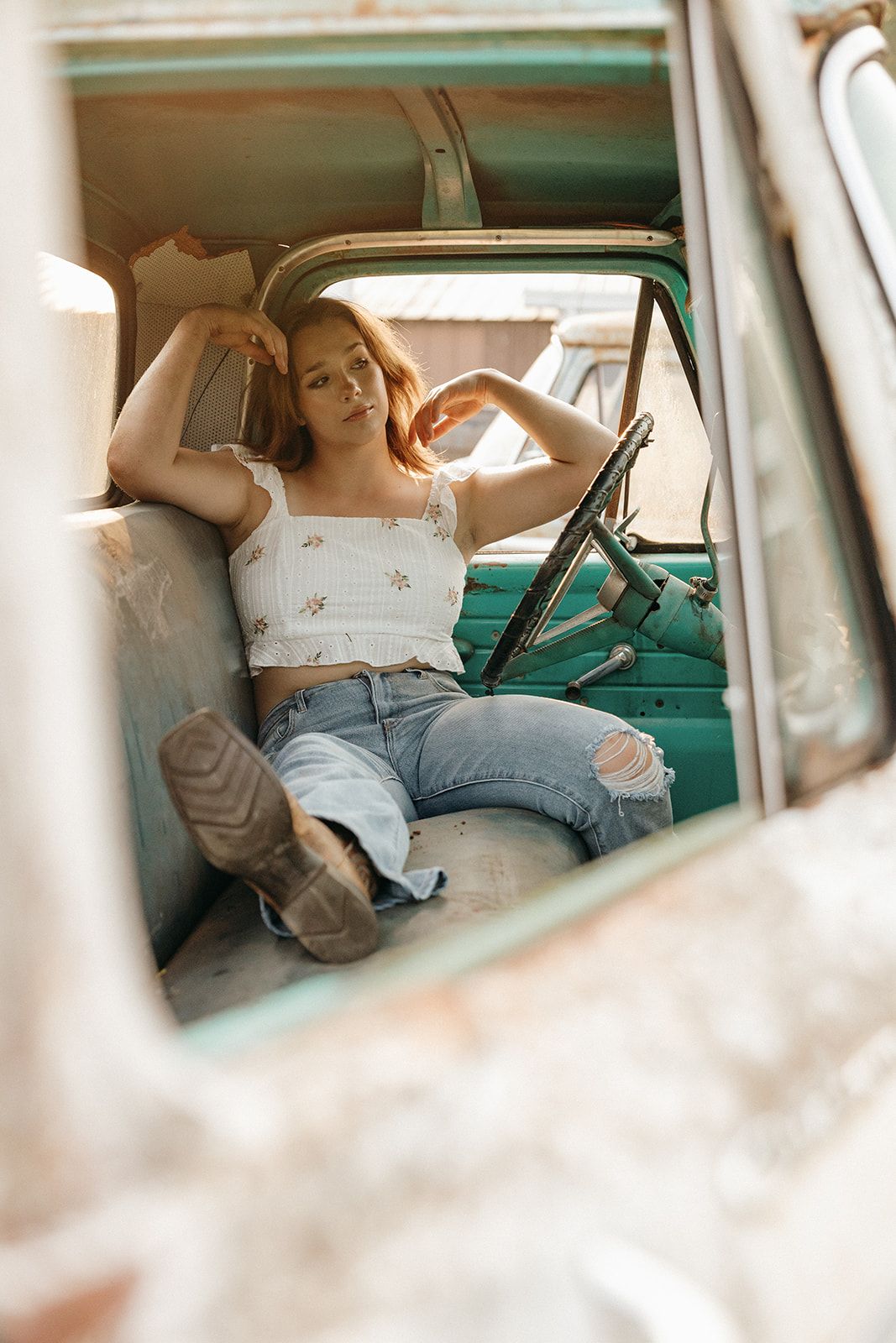 View through car window of person lounging in vintage turquoise vehicle wearing crop top and distressed jeans.