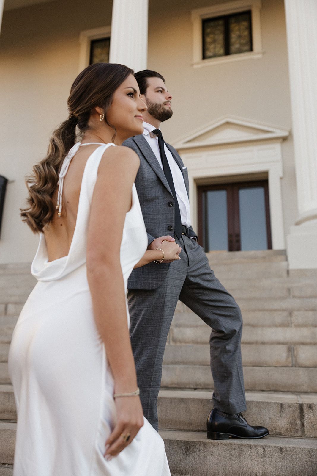 Couple in wedding attire poses on elegant stone steps of classic building.