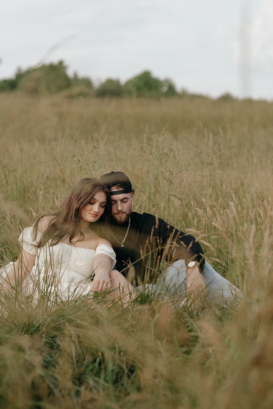 A romantic couple sits intimately together in a golden field of tall grass during sunset.