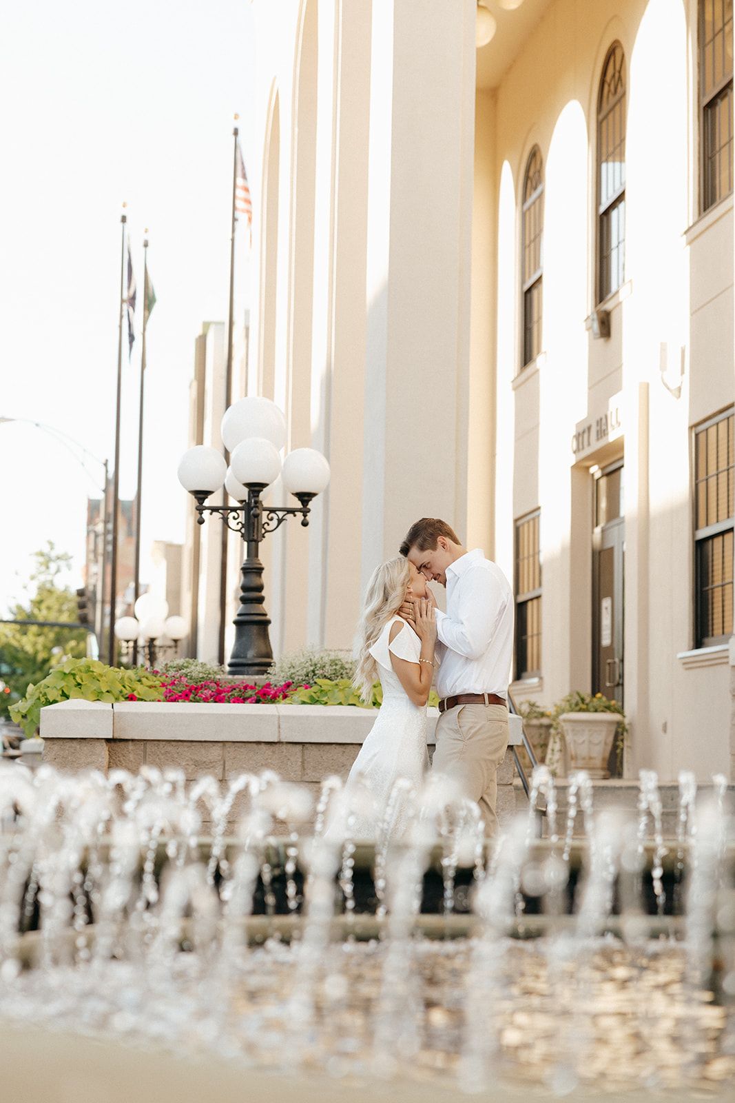 Romantic wedding couple embraces by elegant columns and fountains on a sunny day at their classic venue.