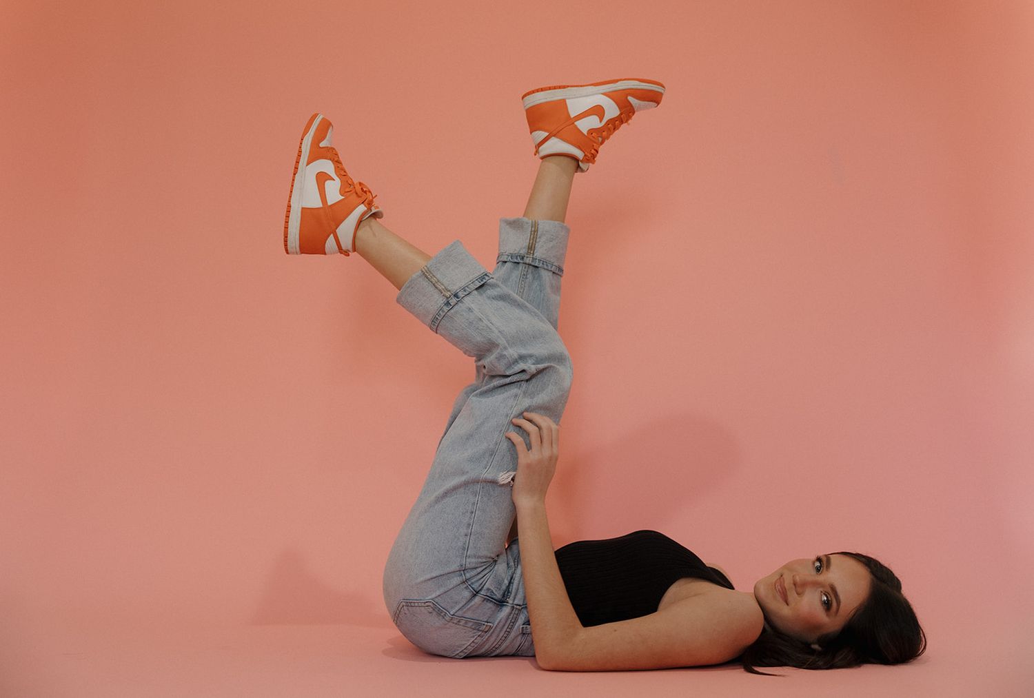 Woman in gray outfit performing acrobatic shoulder stand sequence against coral pink background.