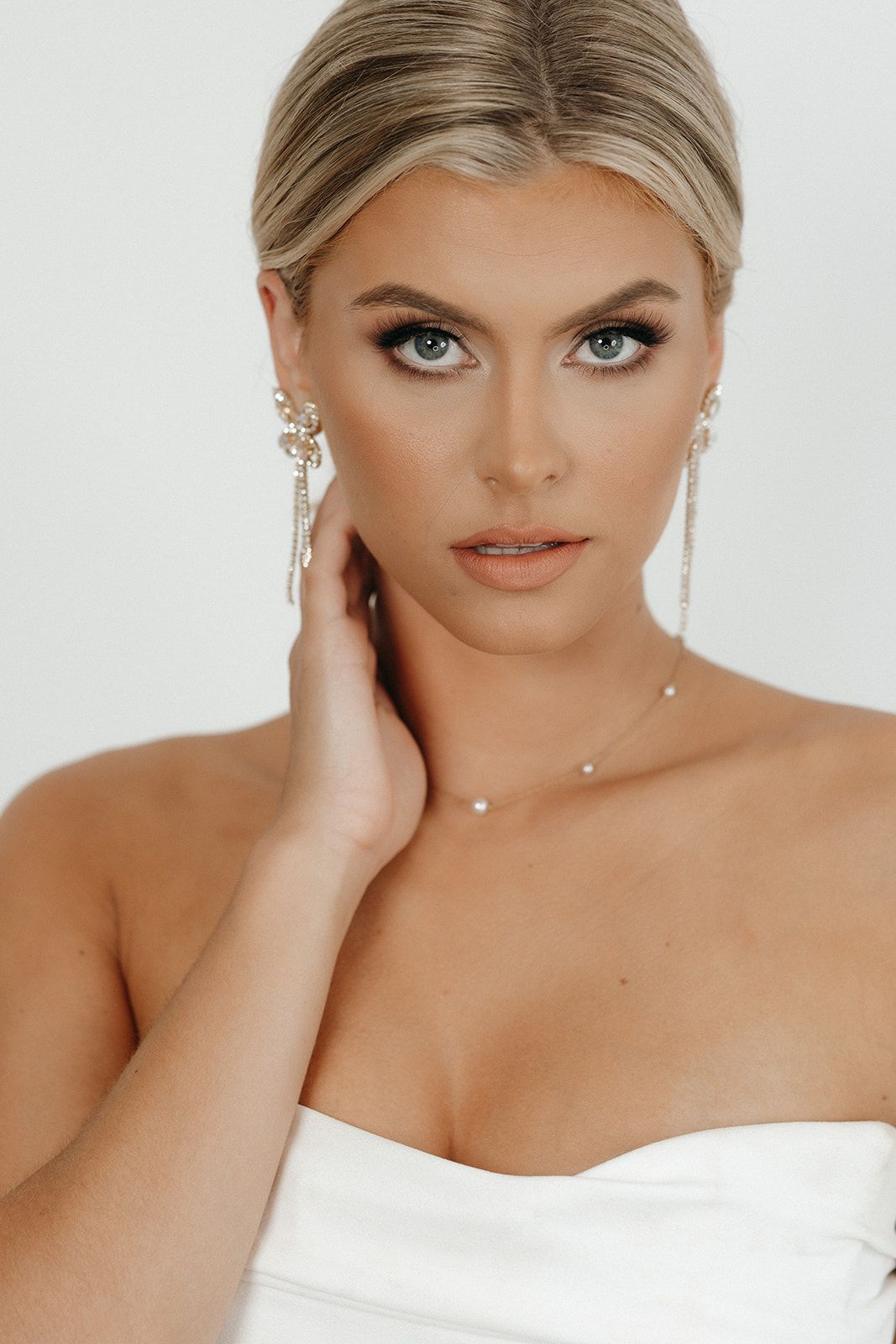Portrait of a bride in a strapless white dress wearing delicate jewelry with elegant makeup and blonde hair.