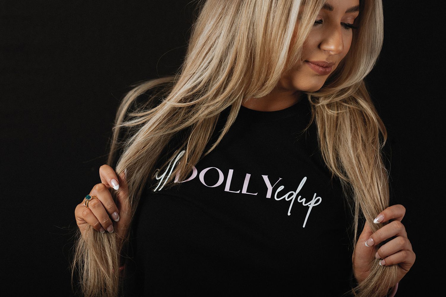 Person wearing a black shirt with 'DOLLY' text on it against dark background with blonde hair flowing.
