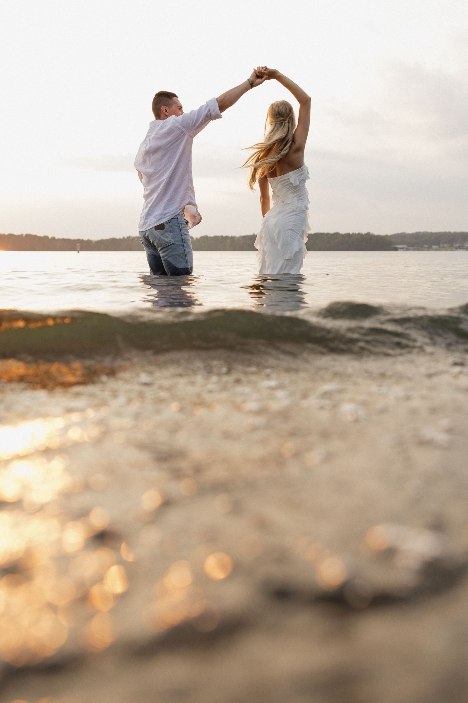Couple dancing in shallow water during golden hour at beach.