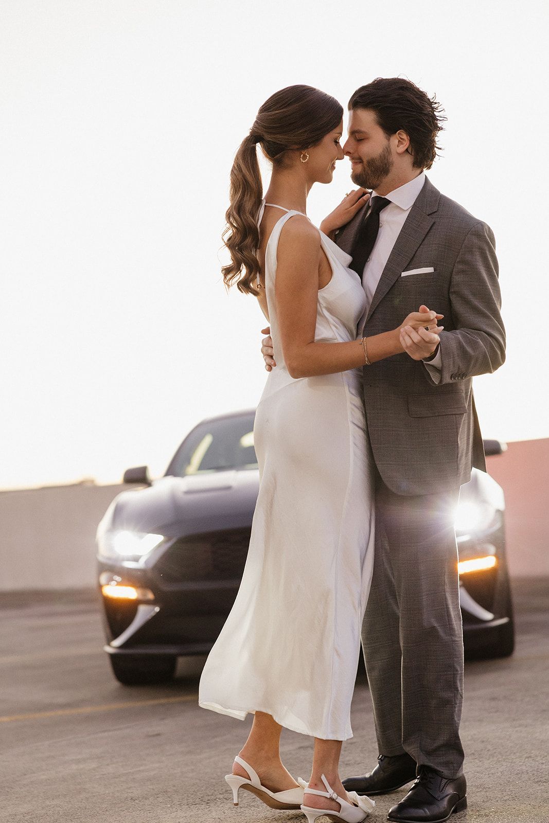 Couple shares romantic dance pose beside luxury car at sunset.