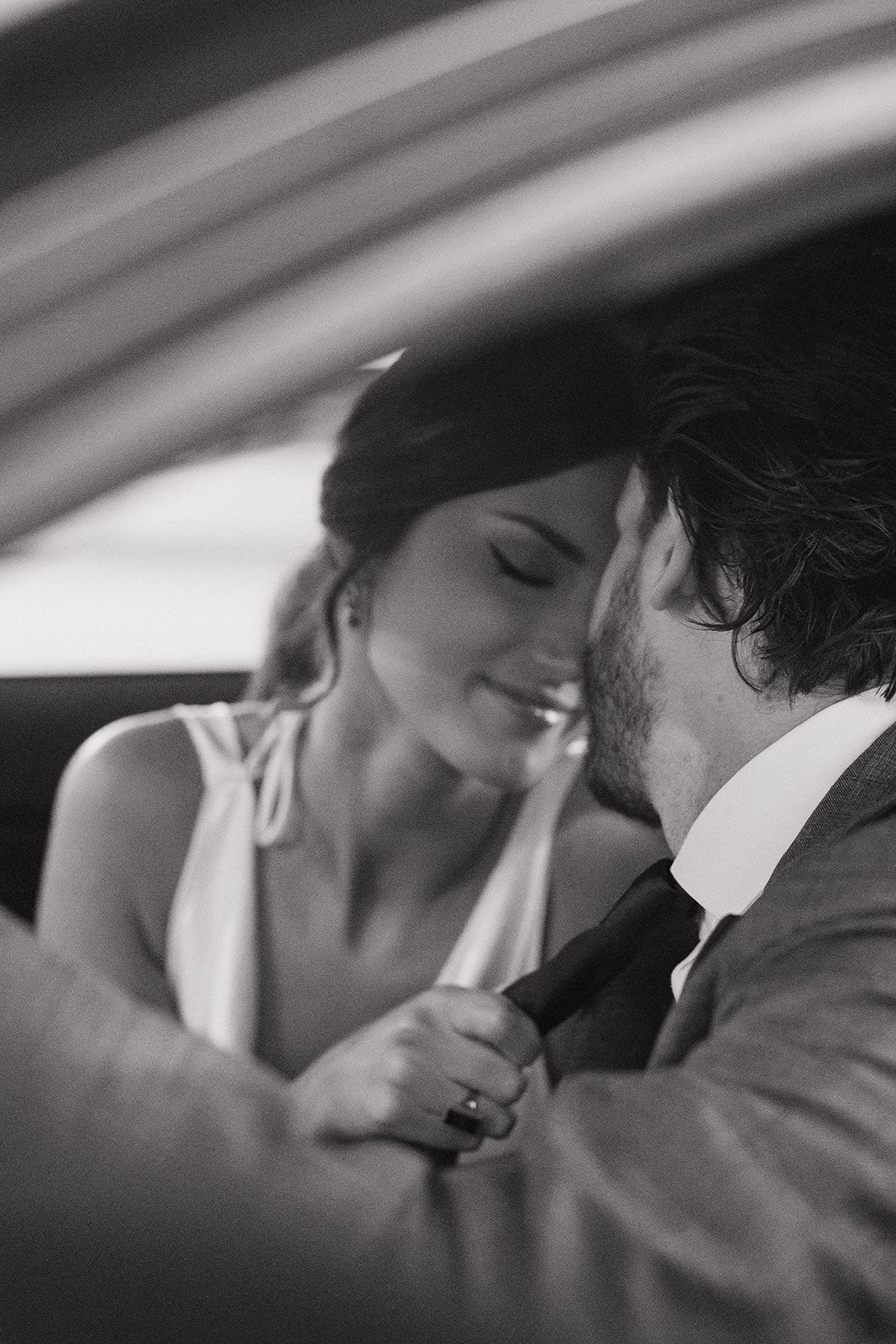 Black and white romantic photo of a couple sharing an intimate moment in a car.