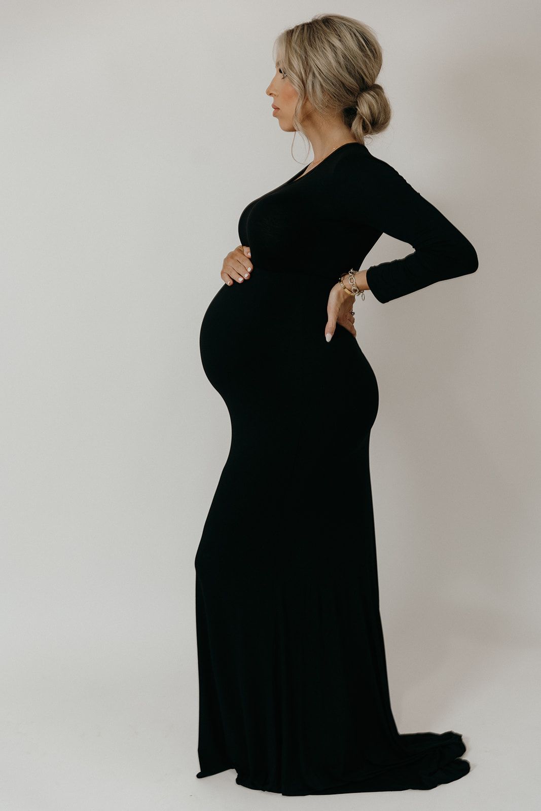 Monochrome maternity photo series showing figure in black dress against white background highlighting the pregnancy silhouette.